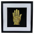 Front-facing gold leaf Hand of Fatima wall art centred on a black background with white mount