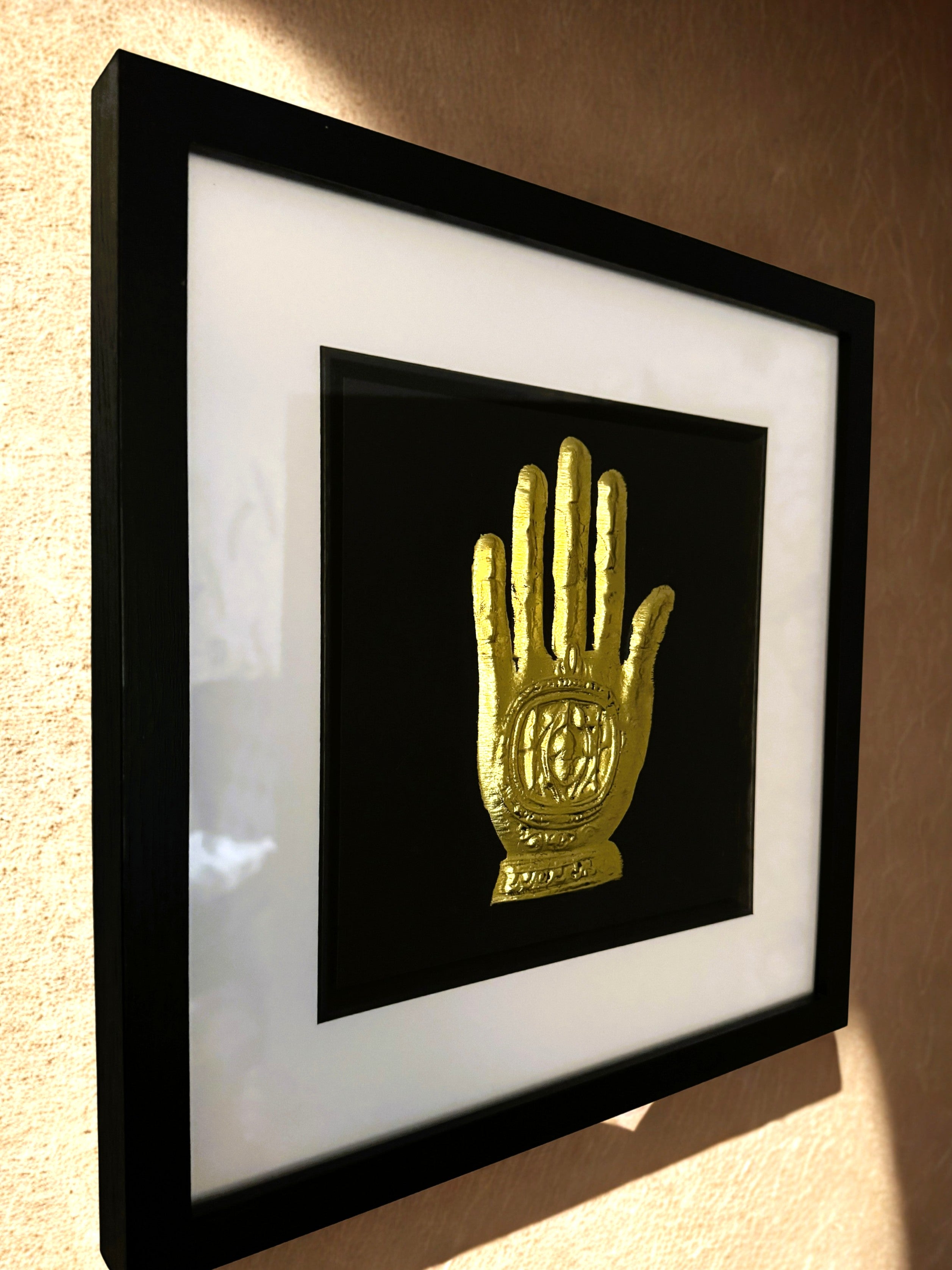 Angled wall-mounted gold leaf Hand of Fatima framed wall art on a textured wall