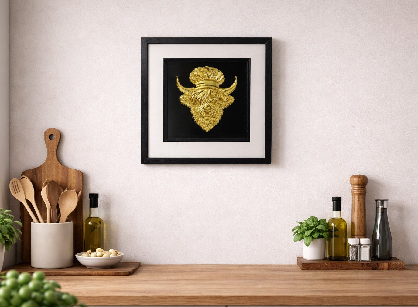 Framed 3D Highland cow chef wall art in gold, styled above a wooden kitchen counter with utensils, herbs, and olive oil bottles.