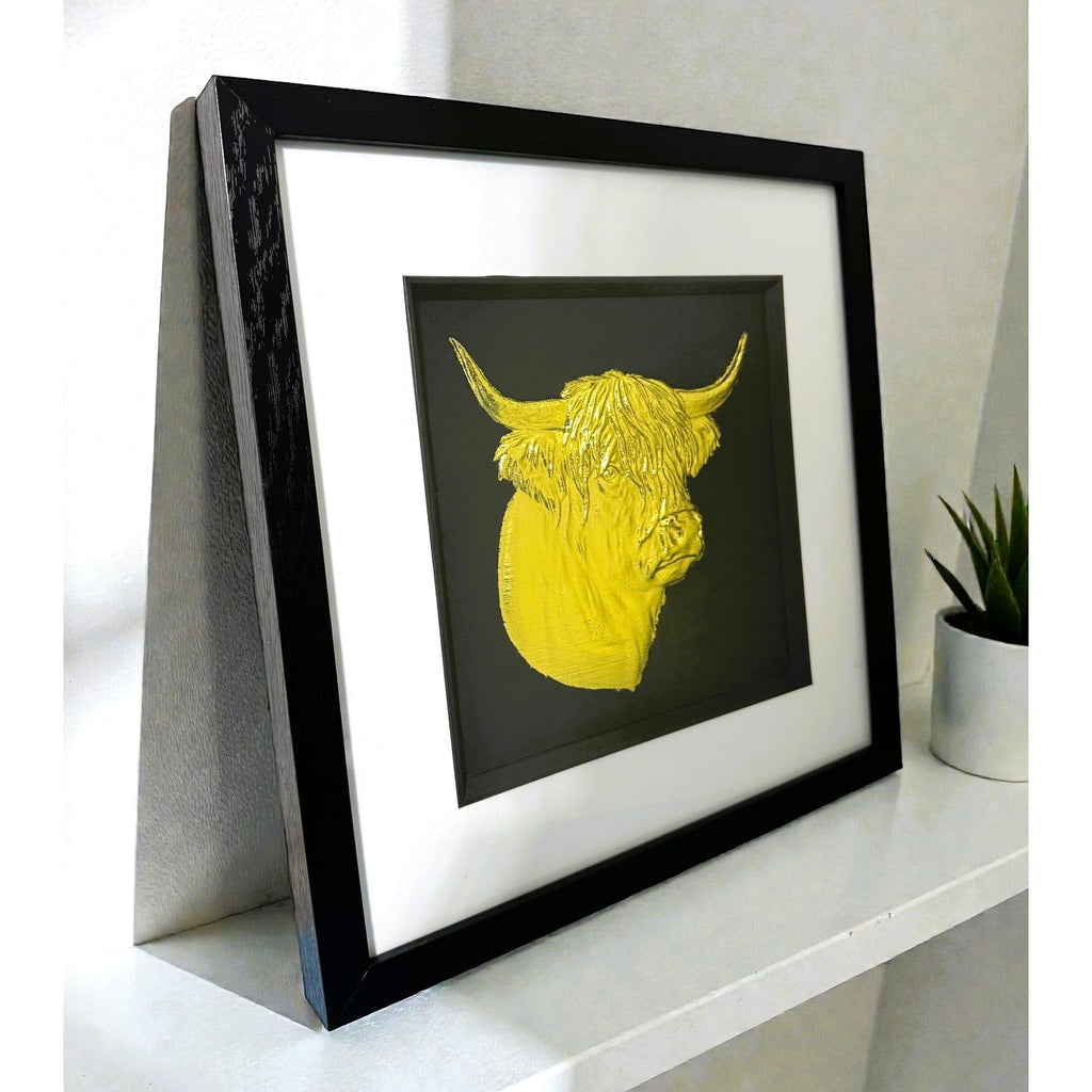 Angled view of gold leaf Highland cow head framed wall art on a white shelf