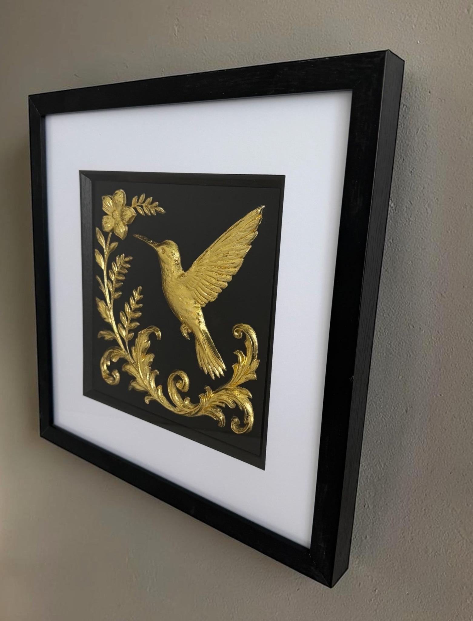 Angled Gold hummingbird artwork on a wall showing the black box frame, white mount and glass front