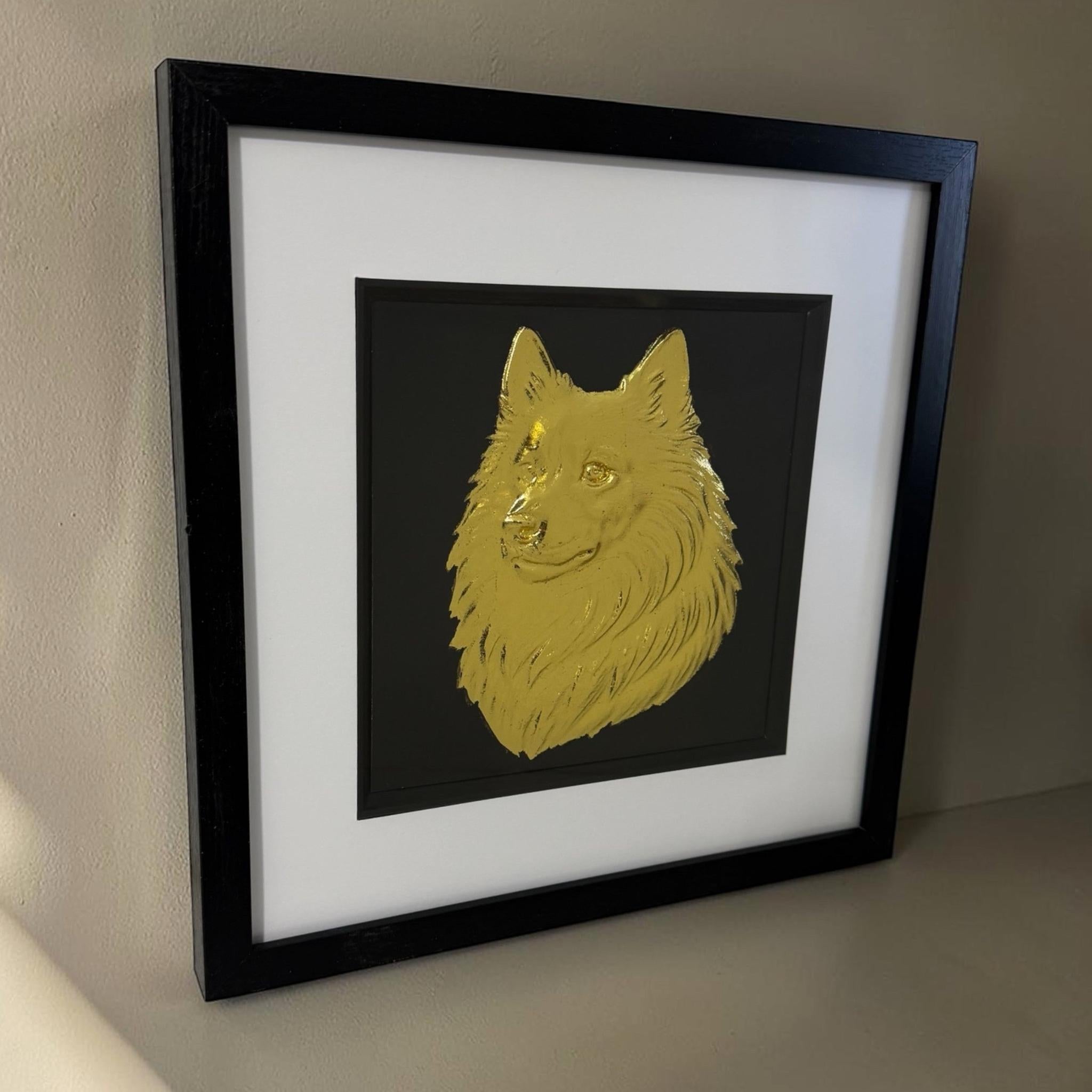 Gold Japanese Spitz relief portrait hanging on a neutral wall in a square black frame with a white mount and black inner surround.