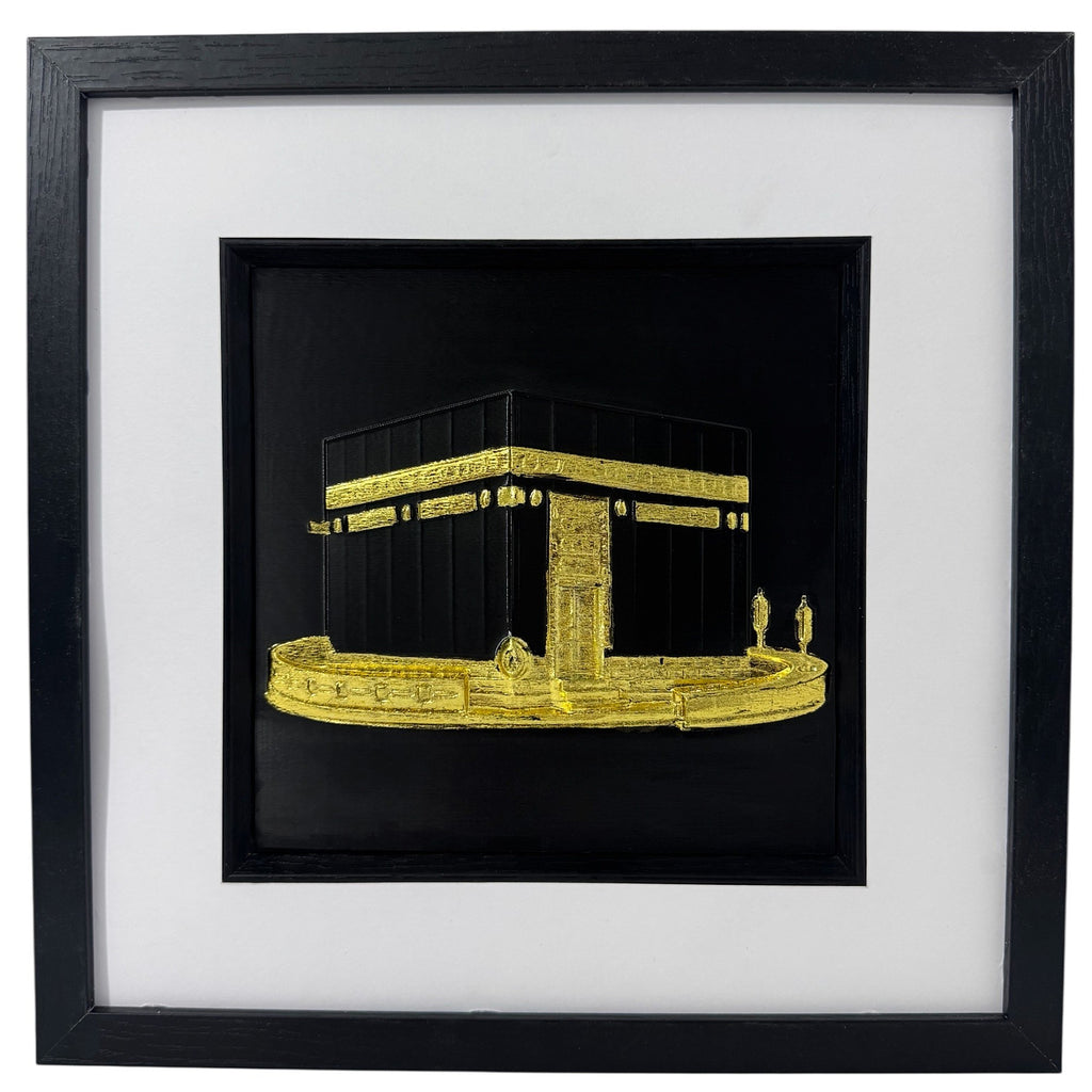 Gold Kaaba relief in a black box frame with wide white mount and black inner surround.