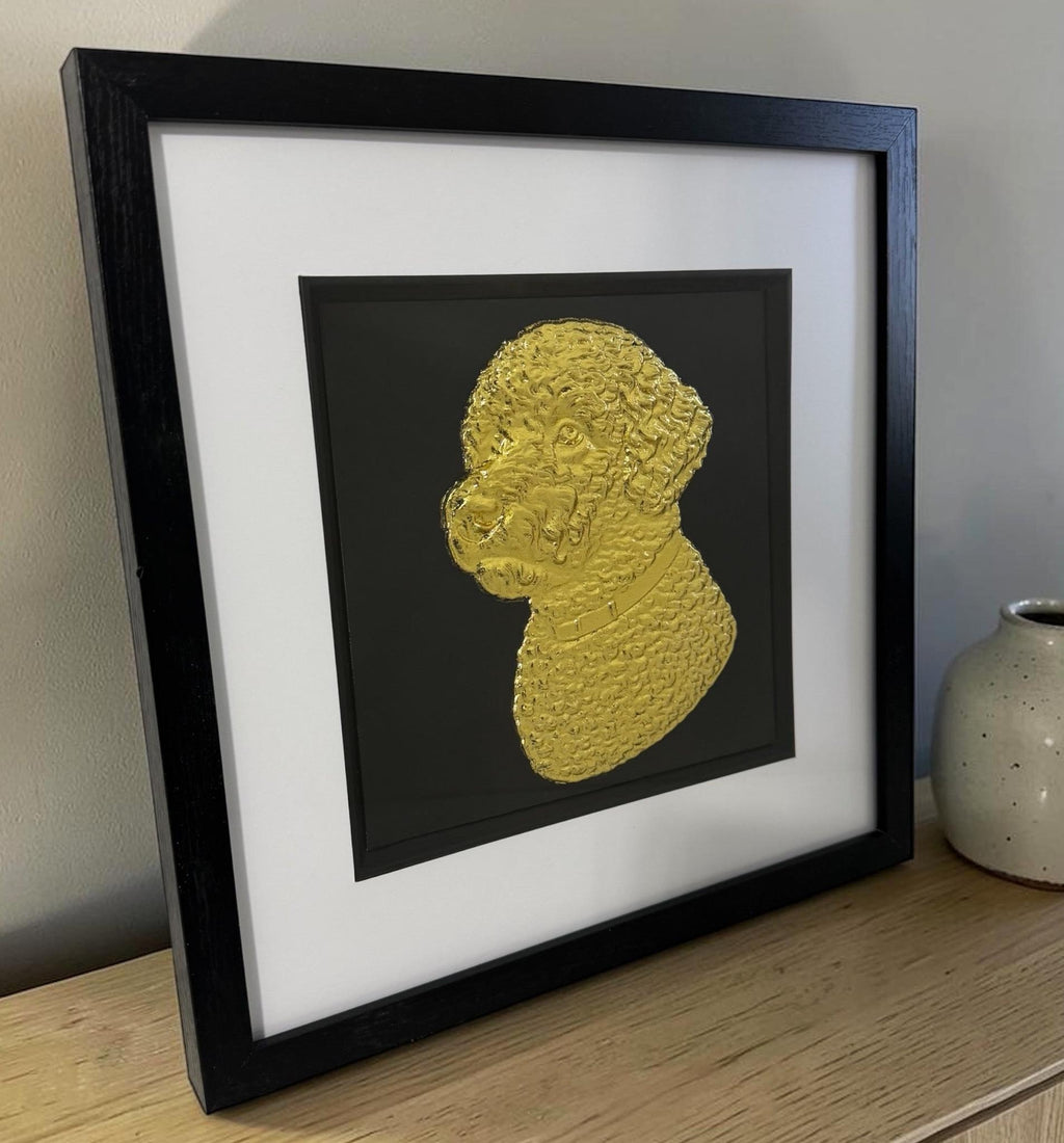 Gold Lagotto Romagnolo relief portrait in a black box frame on a light wood surface beside a ceramic vase.