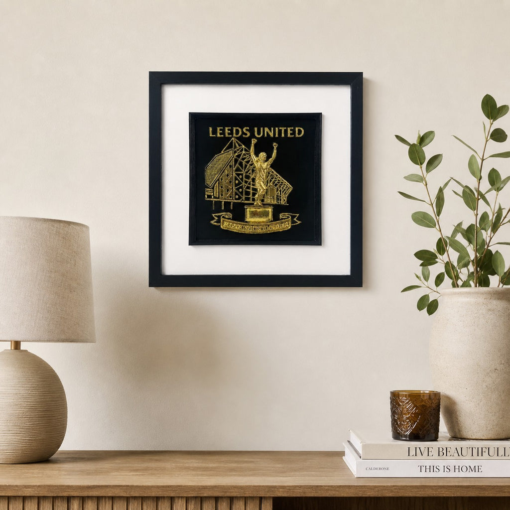Lifestyle photo of Leeds United wall art displayed on a neutral wall above a wooden sideboard with home decor.