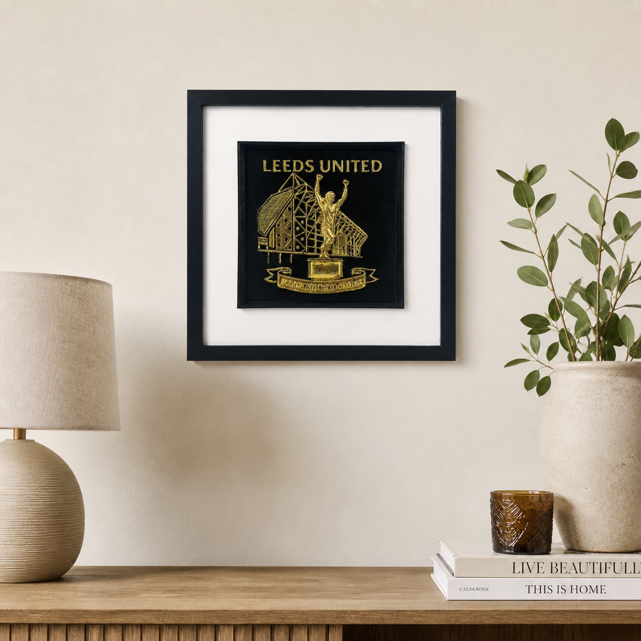 Lifestyle photo of Leeds United wall art displayed on a neutral wall above a wooden sideboard with home decor.