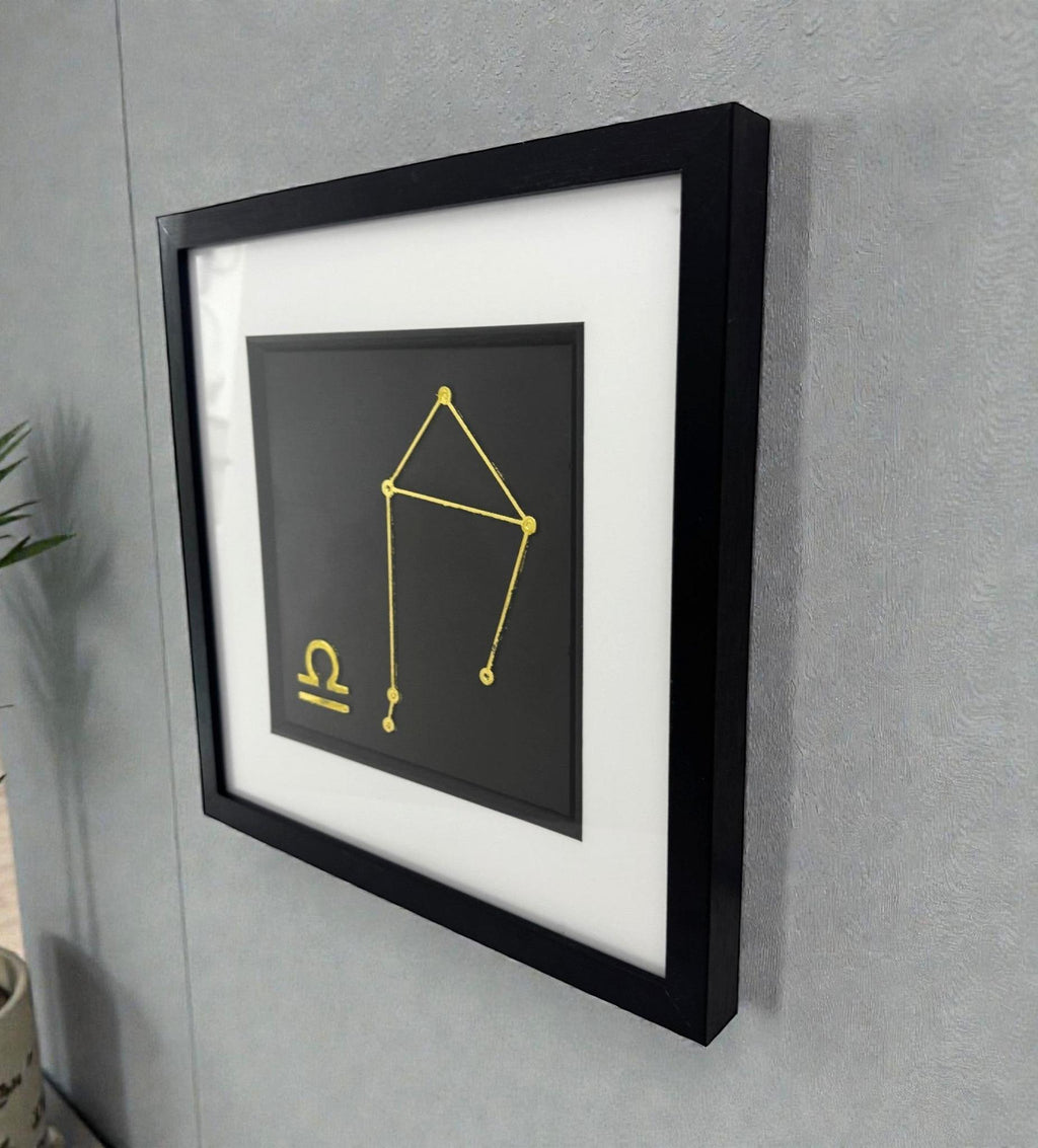 Framed gold Libra constellation wall art displayed on a wall, black frame with white mount and constellation star pattern