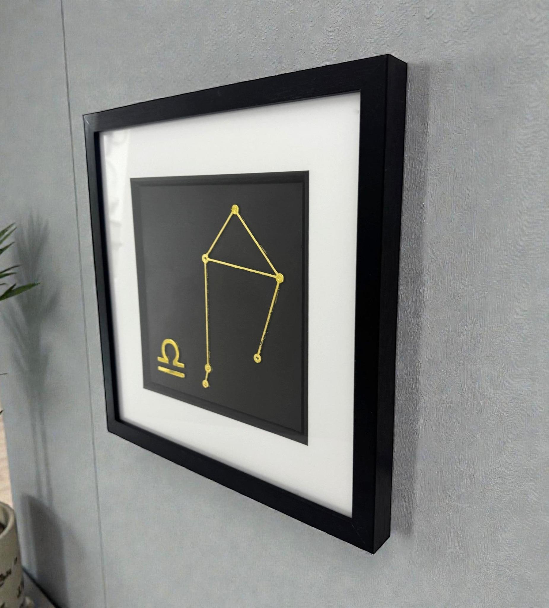 Framed gold Libra constellation wall art displayed on a wall, black frame with white mount and constellation star pattern