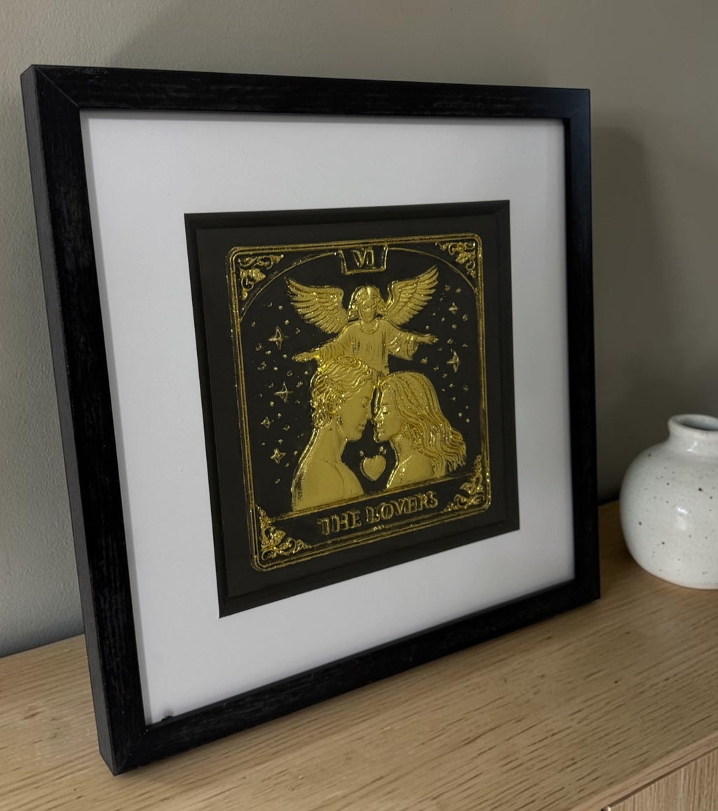 Angled tabletop view of Gold The Lovers tarot raised artwork in black box frame with white mount