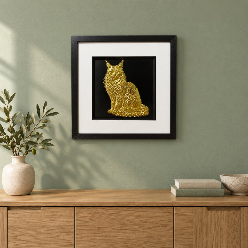 Gold Maine Coon 3D wall art in a black square frame hung on a sage green wall above an oak sideboard with a vase of olive branches, books and a bowl