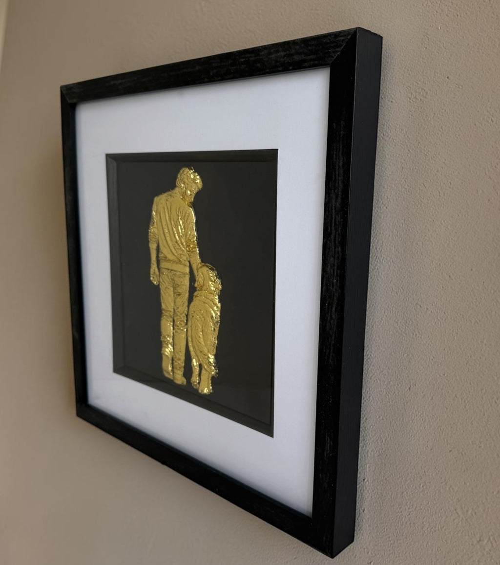 Gold framed man and dog artwork on a neutral wall, showing raised detail and black square frame.
