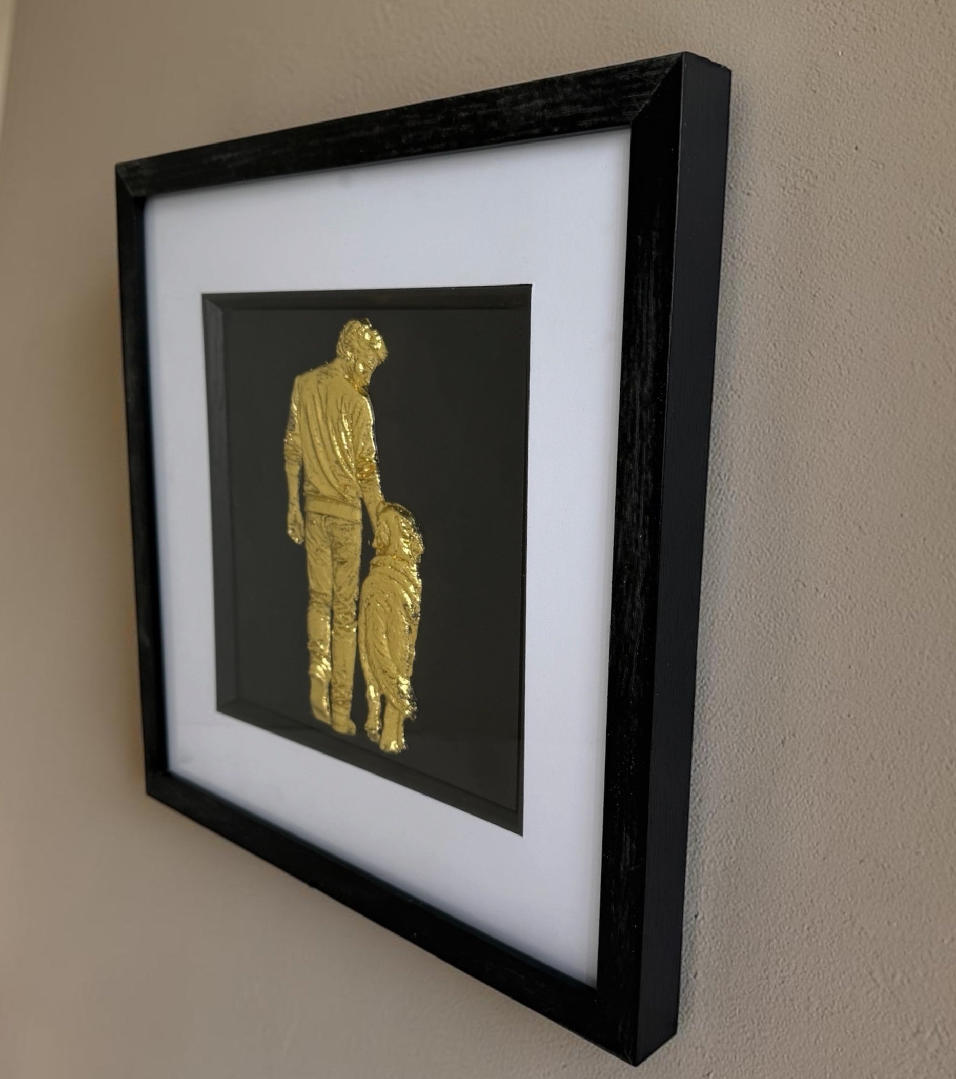 Gold framed man and dog artwork on a neutral wall, showing raised detail and black square frame.