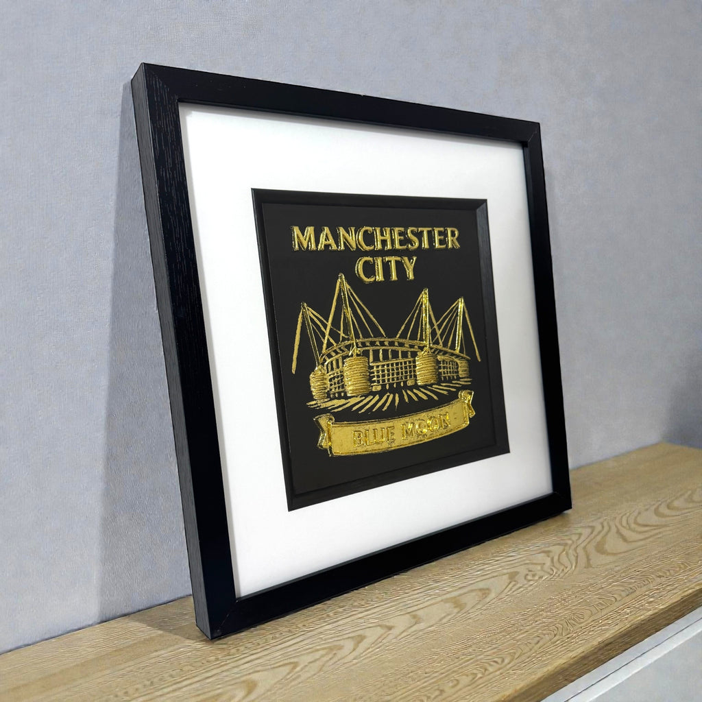 Framed Manchester City gold 3D wall art displayed on a modern wooden shelf.