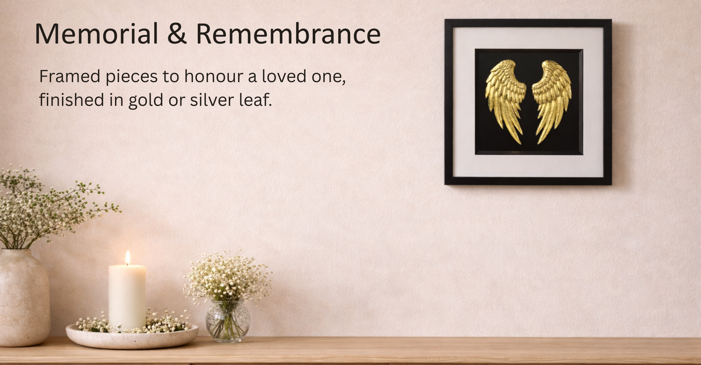 Hero banner for JP Designs Memorial & Remembrance collection showing a framed gold leaf angel wings wall art on a warm beige plaster wall above a light oak console, styled with a candle and baby’s breath flowers, with soft natural light and space for overlay text.