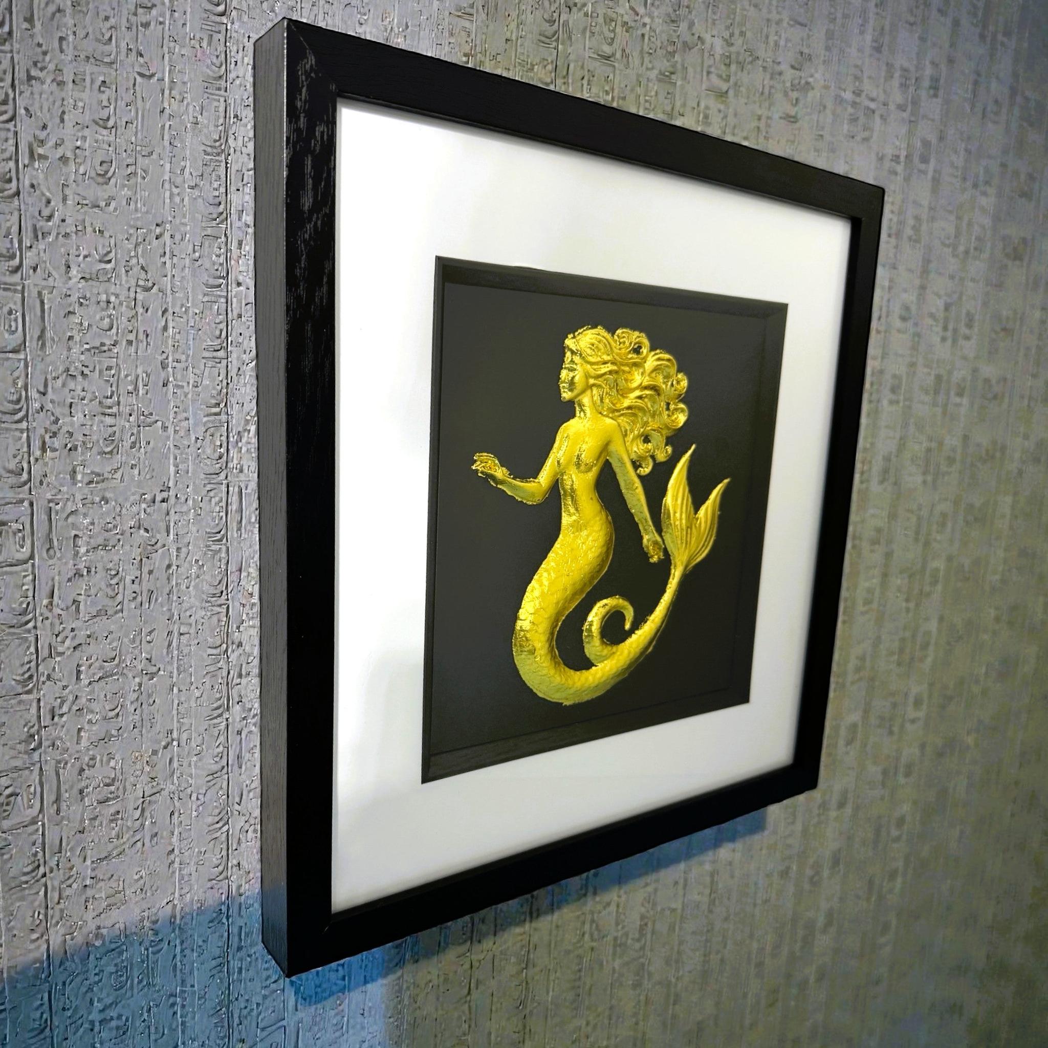 Gold mermaid wall art framed in black hanging on a textured wall