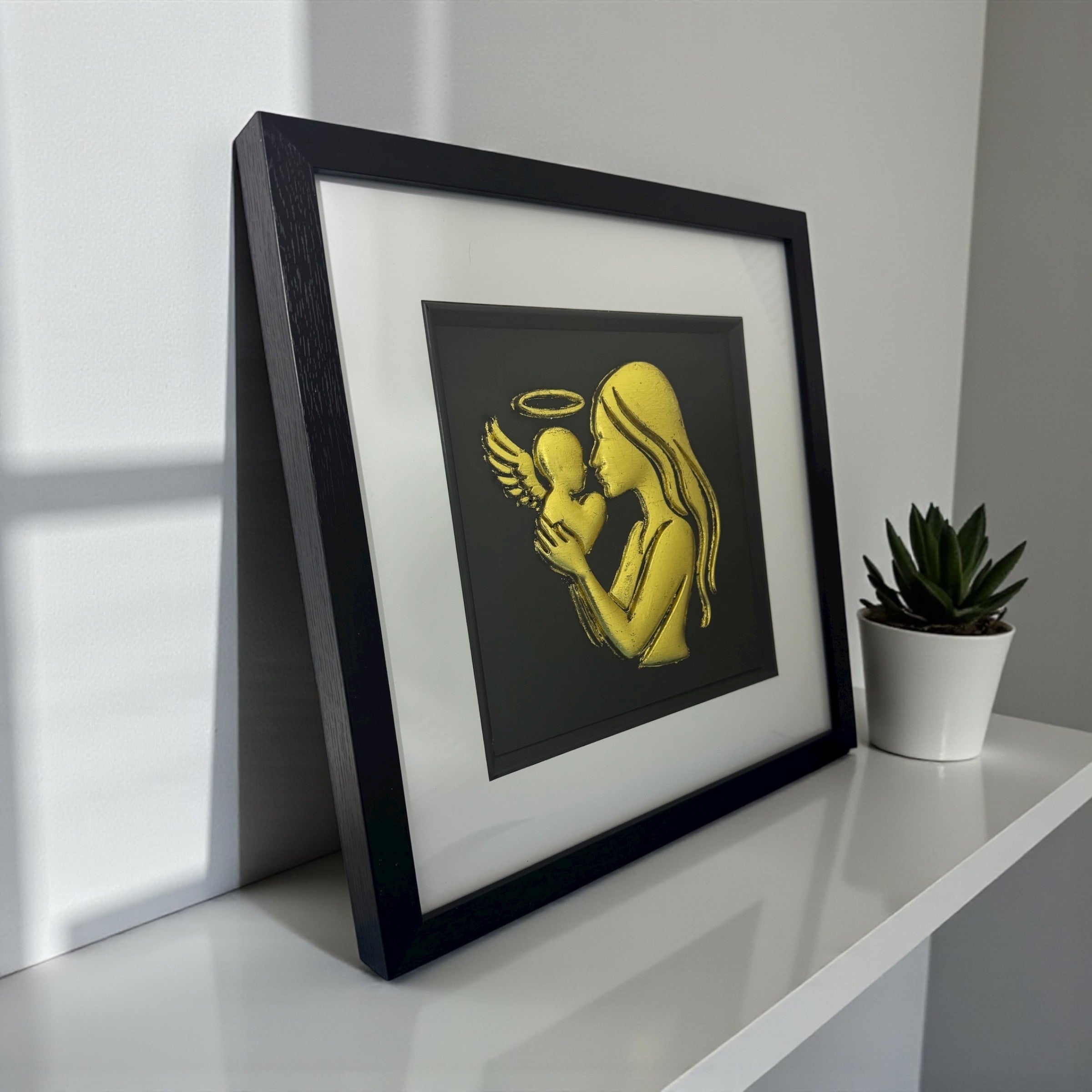 Angled desk view of mother and baby angel framed wall art with silver leaf finish