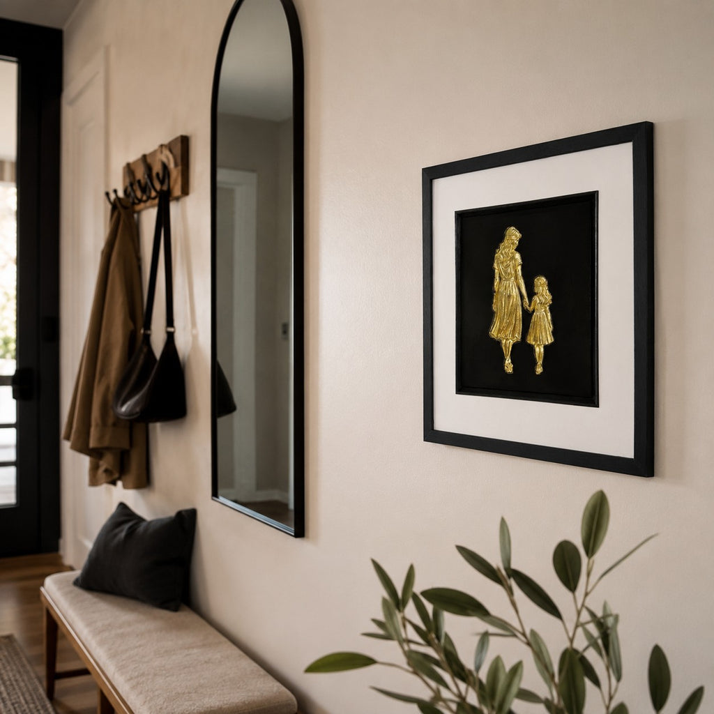 Gold mother and daughter framed artwork styled on a neutral hallway wall near mirror and bench.