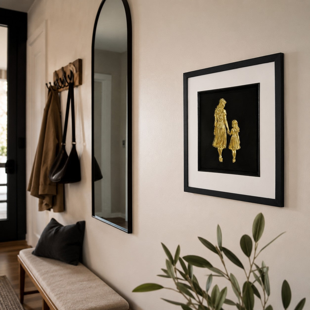 Gold mother and daughter framed artwork styled on a neutral hallway wall near mirror and bench.