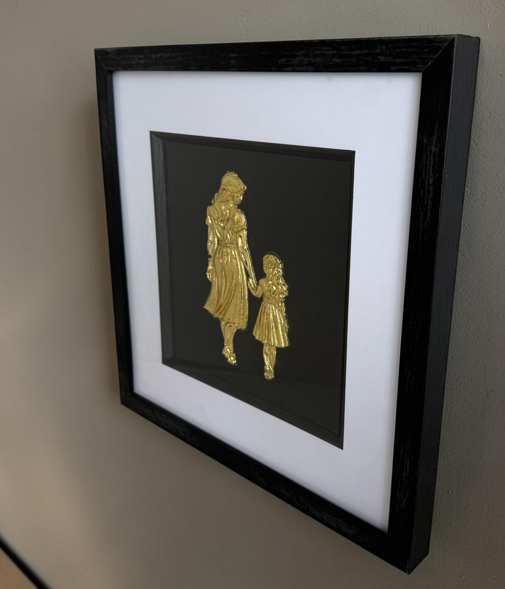 Angled wall view of Gold mother and daughter raised relief artwork showing black box frame depth.