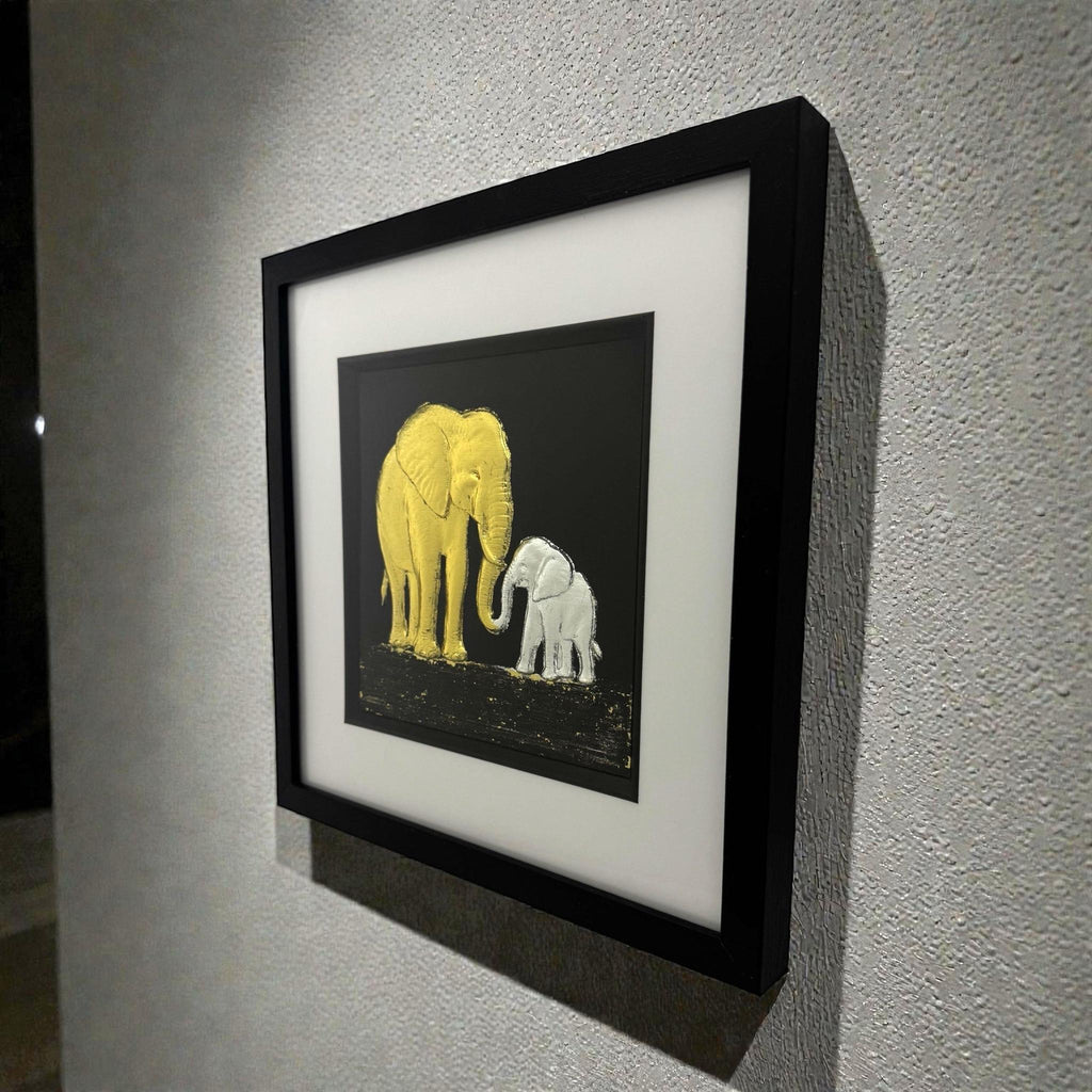Framed elephant mother and baby wall art mounted on a wall, shown at an angle highlighting depth and texture
