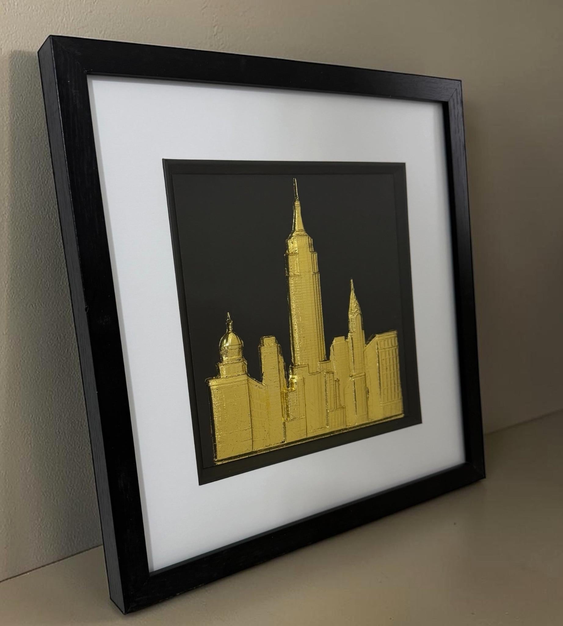 Gold framed New York skyline artwork leaning on a neutral surface with black box frame, white mount and glass front.