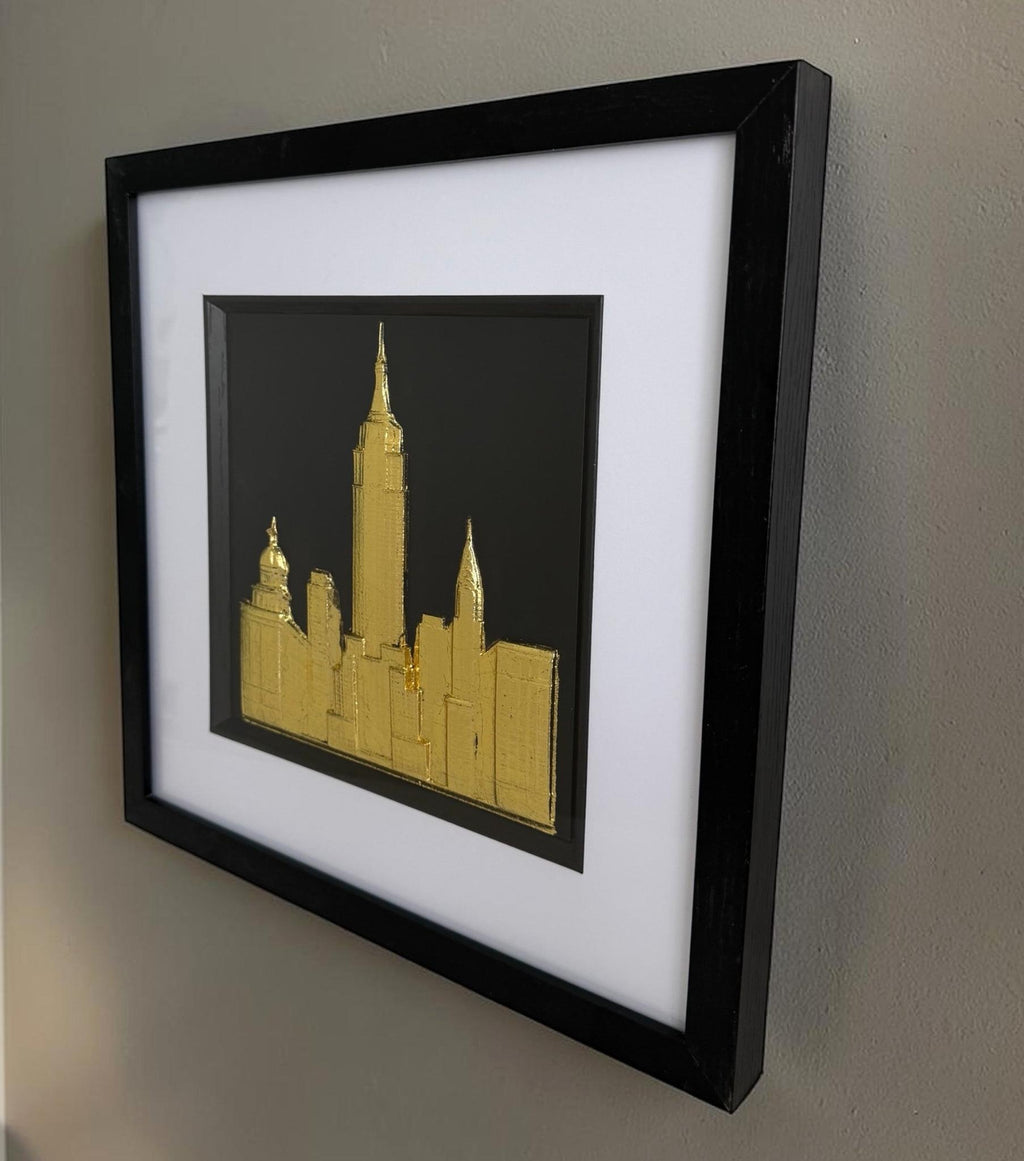 Angled gold New York cityscape artwork on a wall showing raised skyline relief and deep black frame.