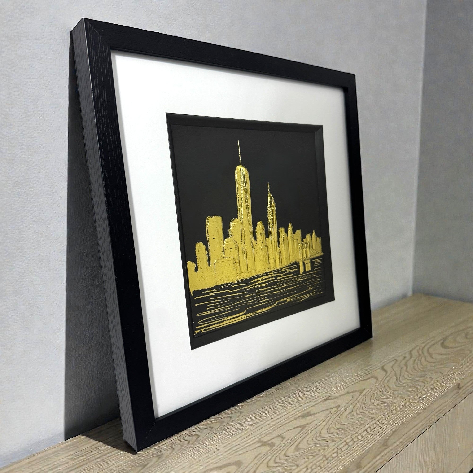 Angled view of gold leaf New York skyline wall art showing frame depth, raised relief texture, and metallic highlights
