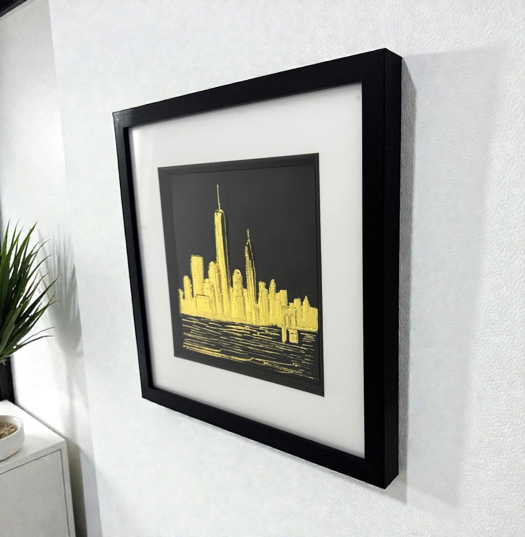 Gold leaf New York skyline wall art displayed on a wall, angled perspective showing scale, shadow depth, and framed finish