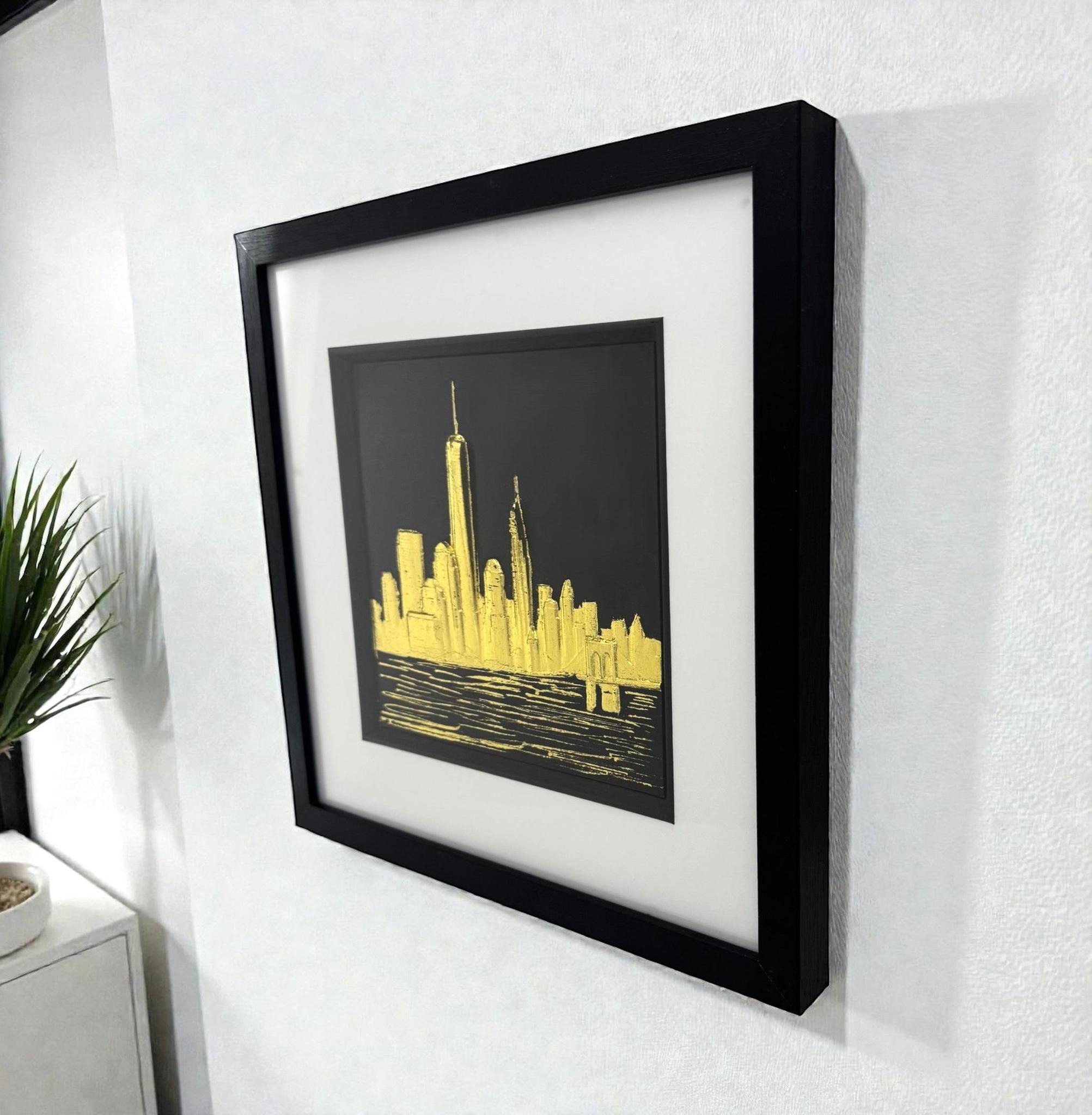 Gold leaf New York skyline wall art displayed on a wall, angled perspective showing scale, shadow depth, and framed finish