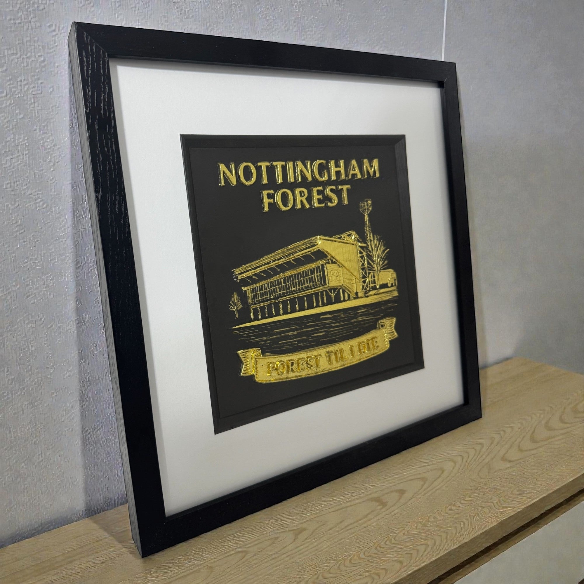 Nottingham Forest framed 3D stadium relief wall art in gold leaf, black box frame with white mount, angled view on shelf.