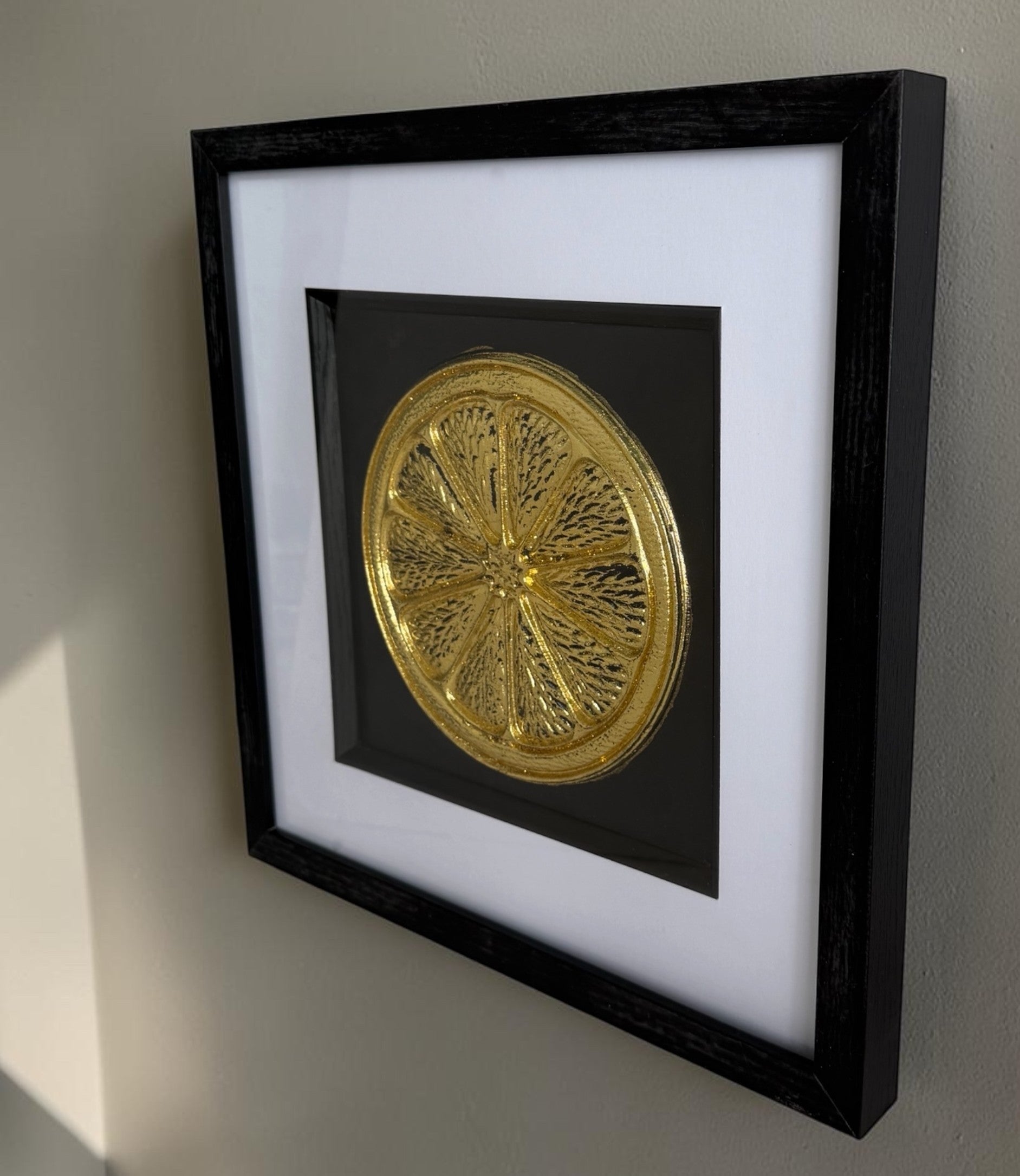 Angled Gold orange slice framed artwork showing raised relief detail, glass front and black box frame.