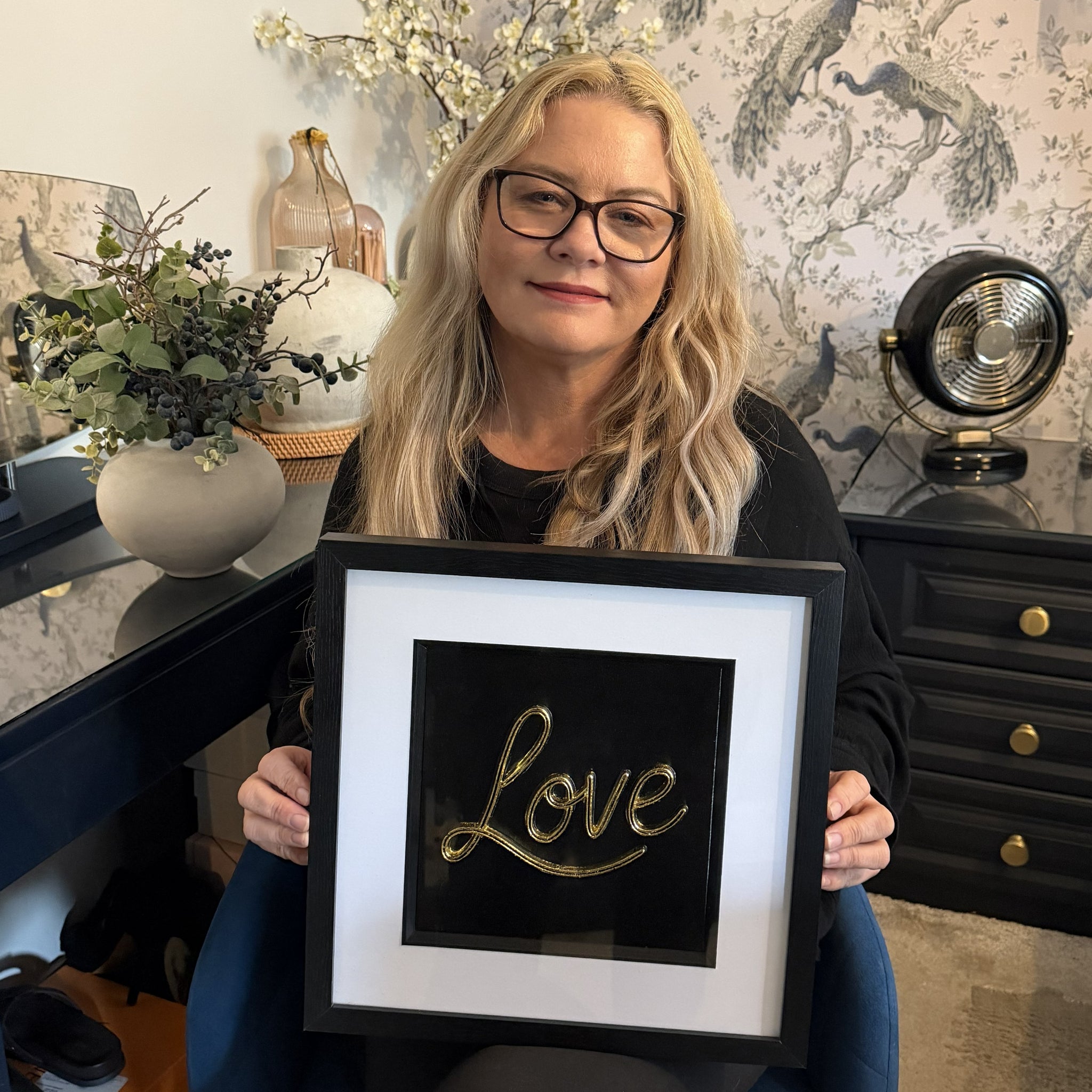 Paula from JP Designs holding handmade framed Love wall art finished in gold leaf in a styled home interior