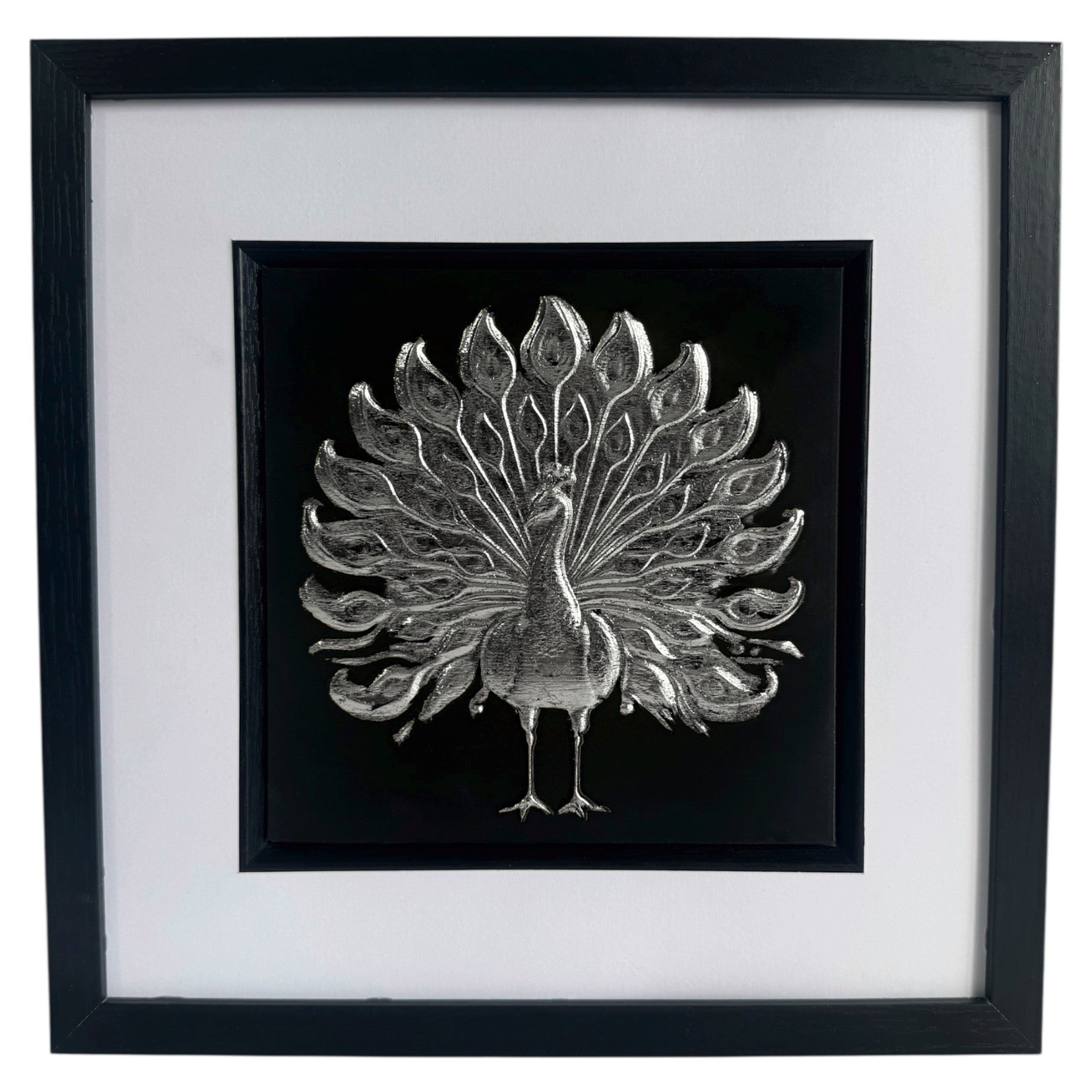 Silver peacock wall art framed in black with white mount on a light wall