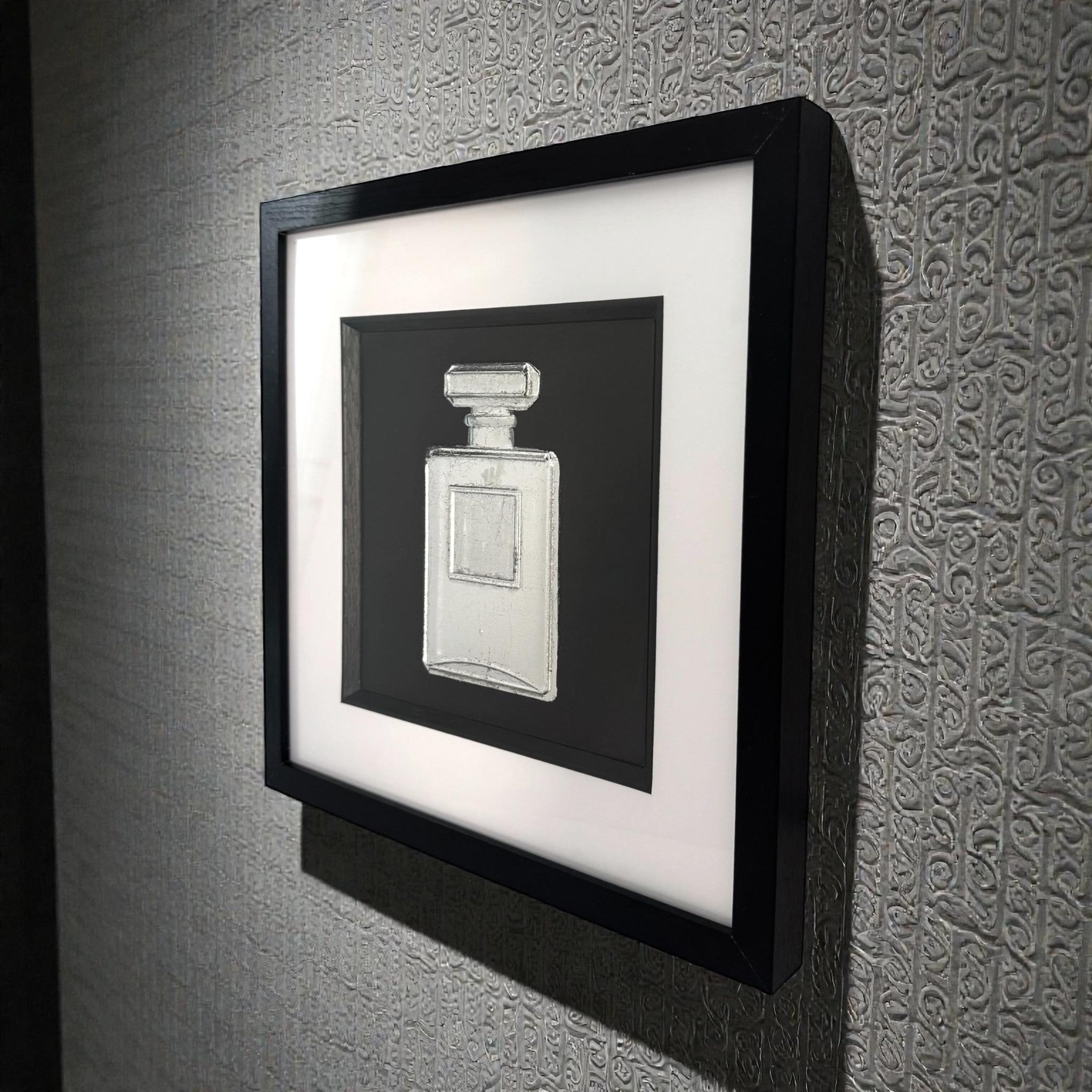 Perfume bottle wall art in silver leaf mounted on a wall, shown in a black frame with white mount