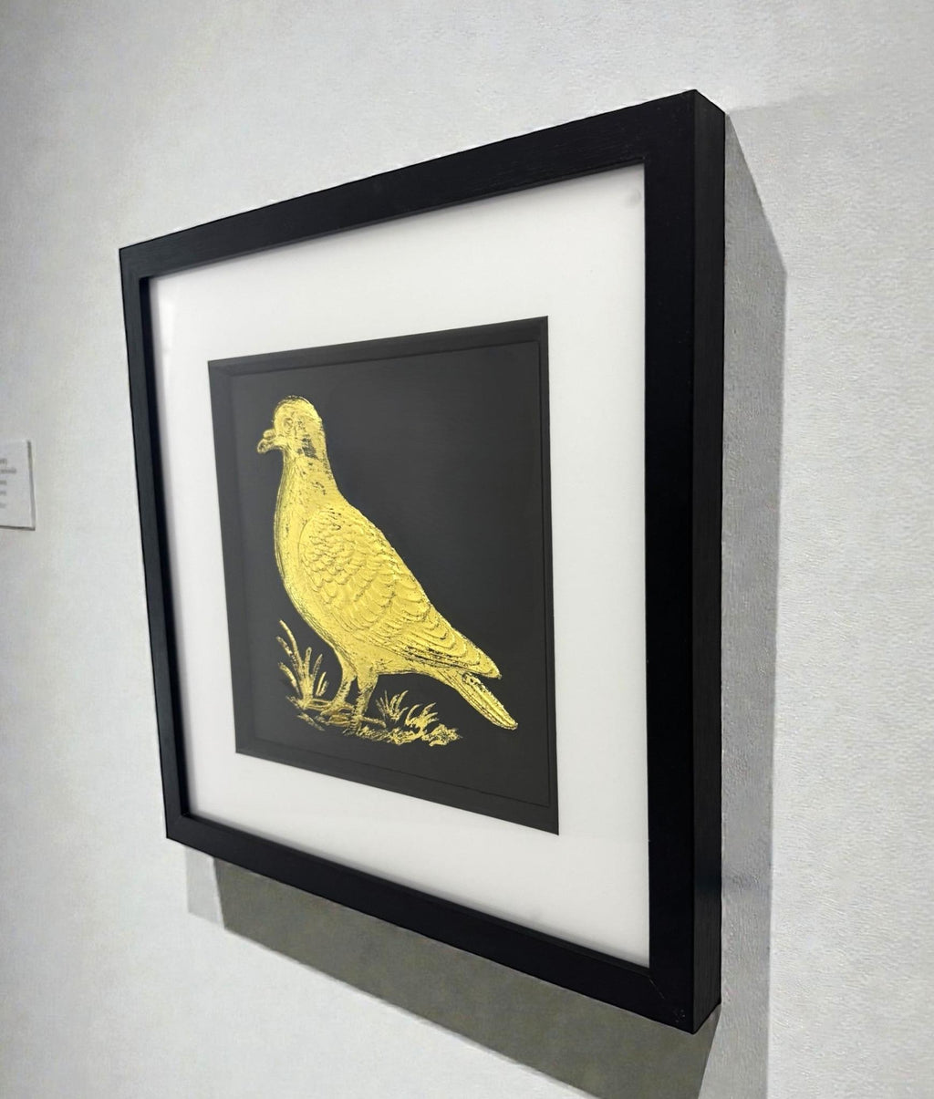 Gold leaf pigeon wall art displayed on a wall, angled perspective showing scale, shadow depth, and framed finish