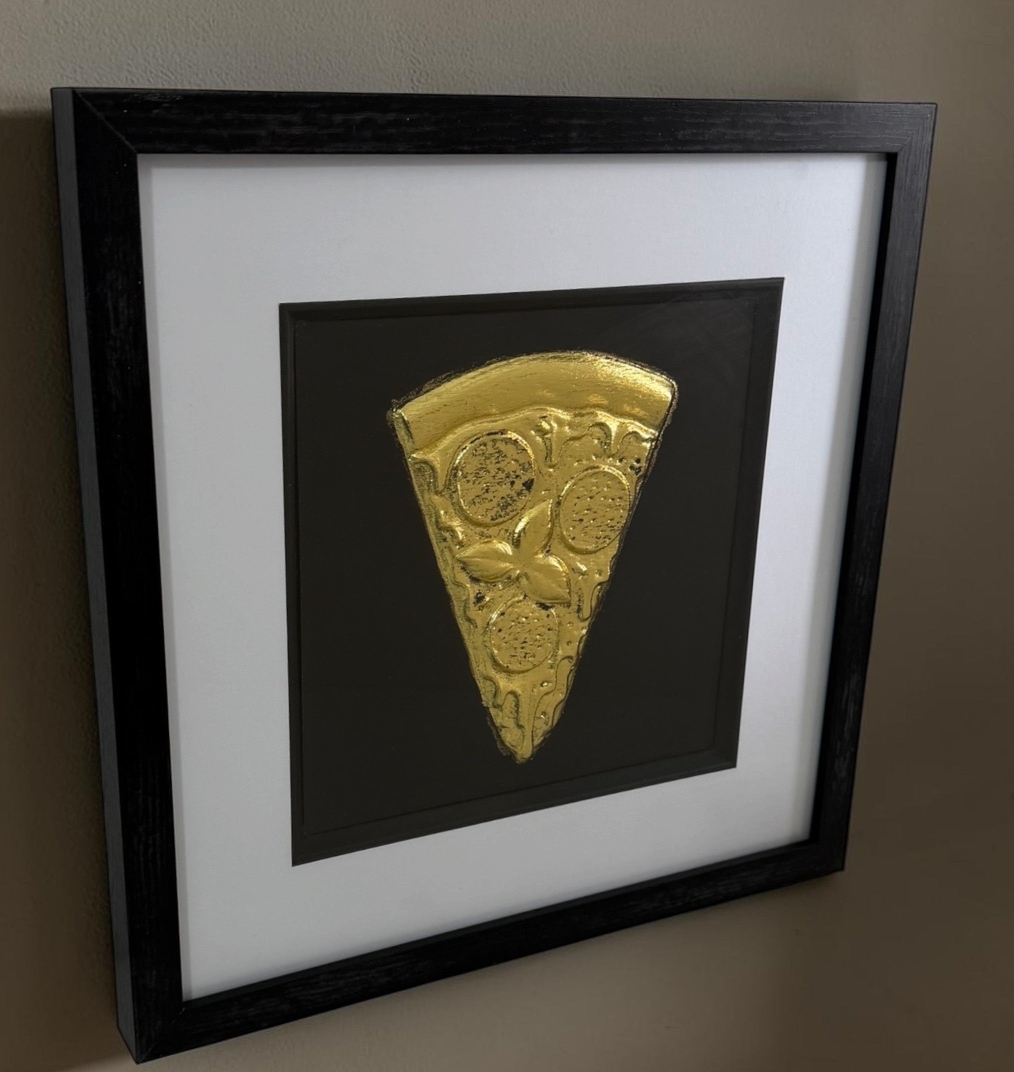 Angled Gold pizza slice framed artwork showing raised relief detail, black background and white mount.