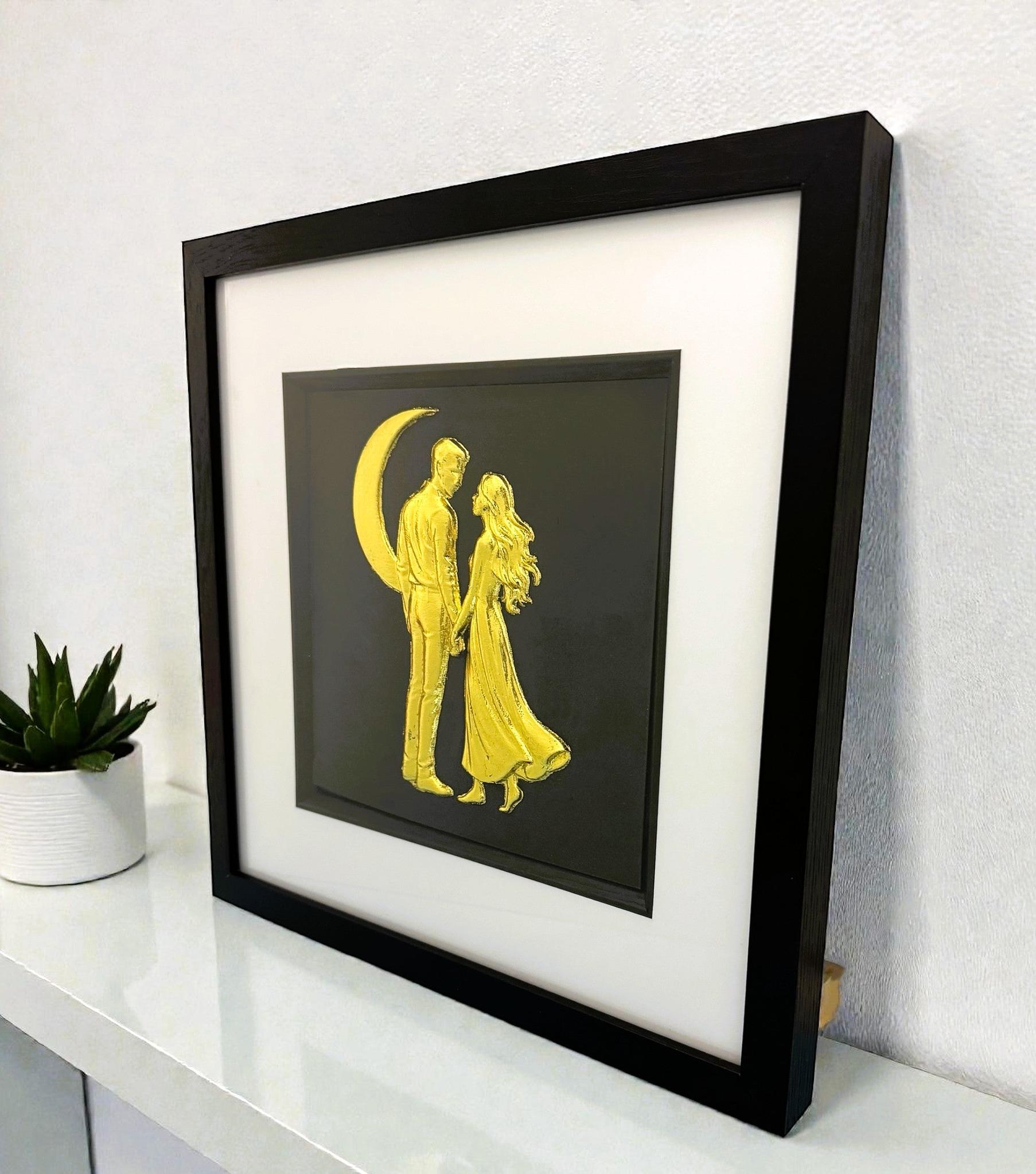 Angled desk view of gold leaf romantic couple under the moon wall art in a black wooden frame