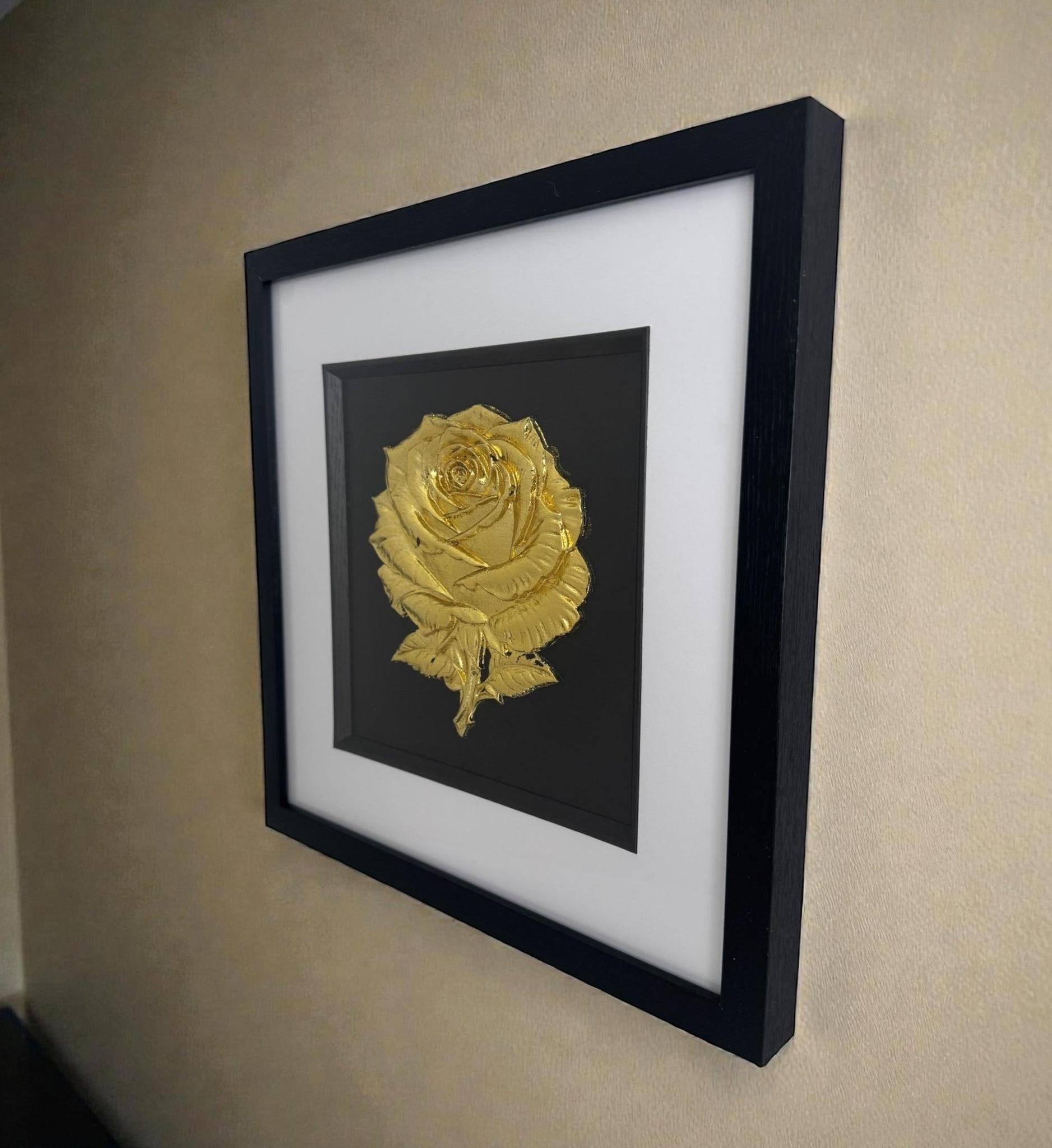 Wall-hung lifestyle photo of framed 3D relief rose in Gold Leaf, black box frame with crisp white mount, shown on a neutral wall.