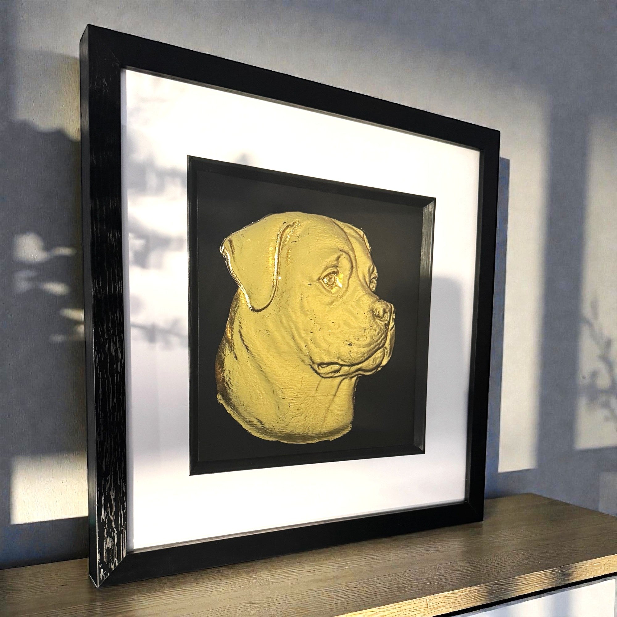 Rottweiler gold leaf wall art photographed at an angle on a shelf with black frame and white mount