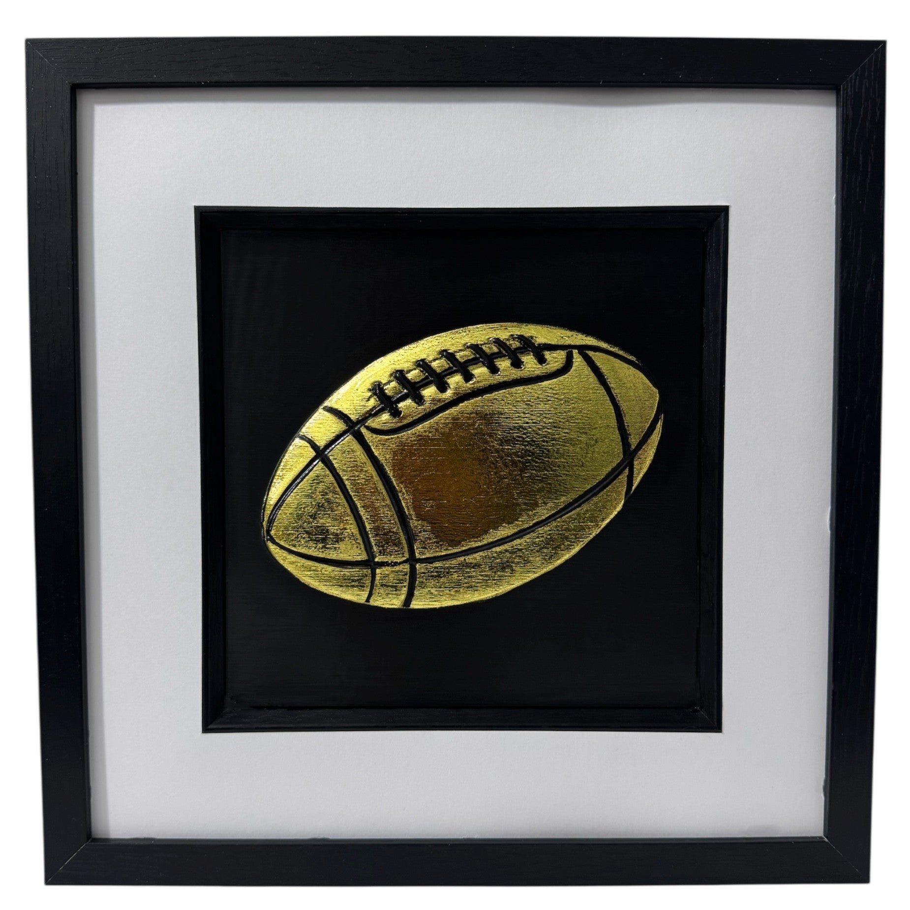 Front view of rugby ball relief artwork in Gold Leaf on black background in a black box frame with white mount