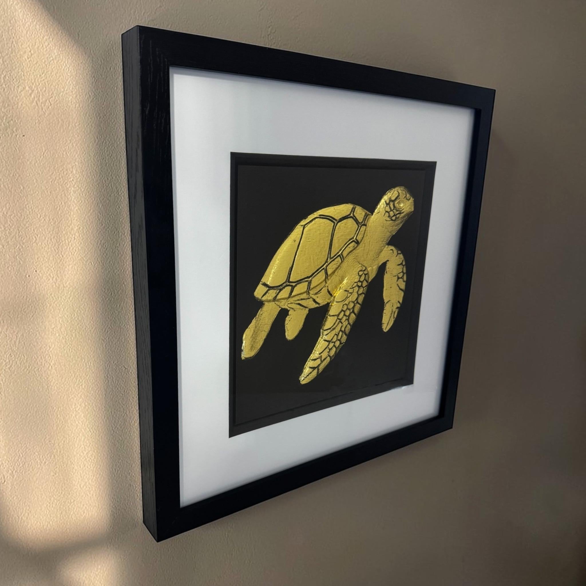 Angled gold framed sea turtle relief on a neutral wall with warm sunlight across the frame