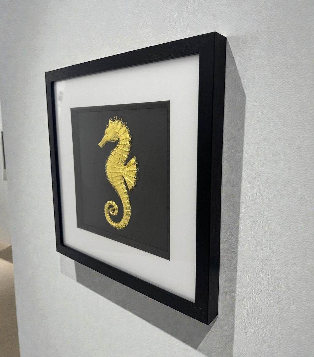 Framed gold seahorse wall art displayed on a wall, black frame with white mount and sculpted marine design