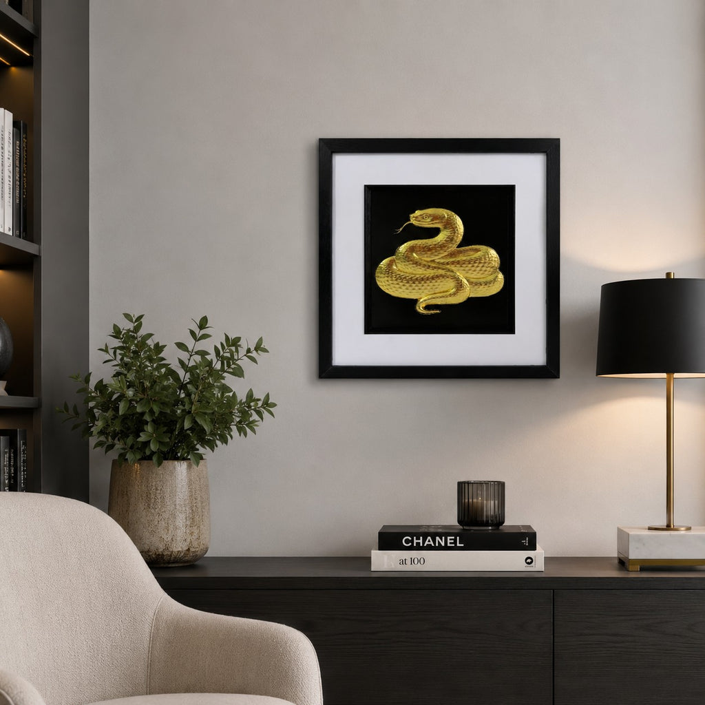 Gold snake artwork styled on a neutral wall above a dark sideboard with lamp, books and plant.
