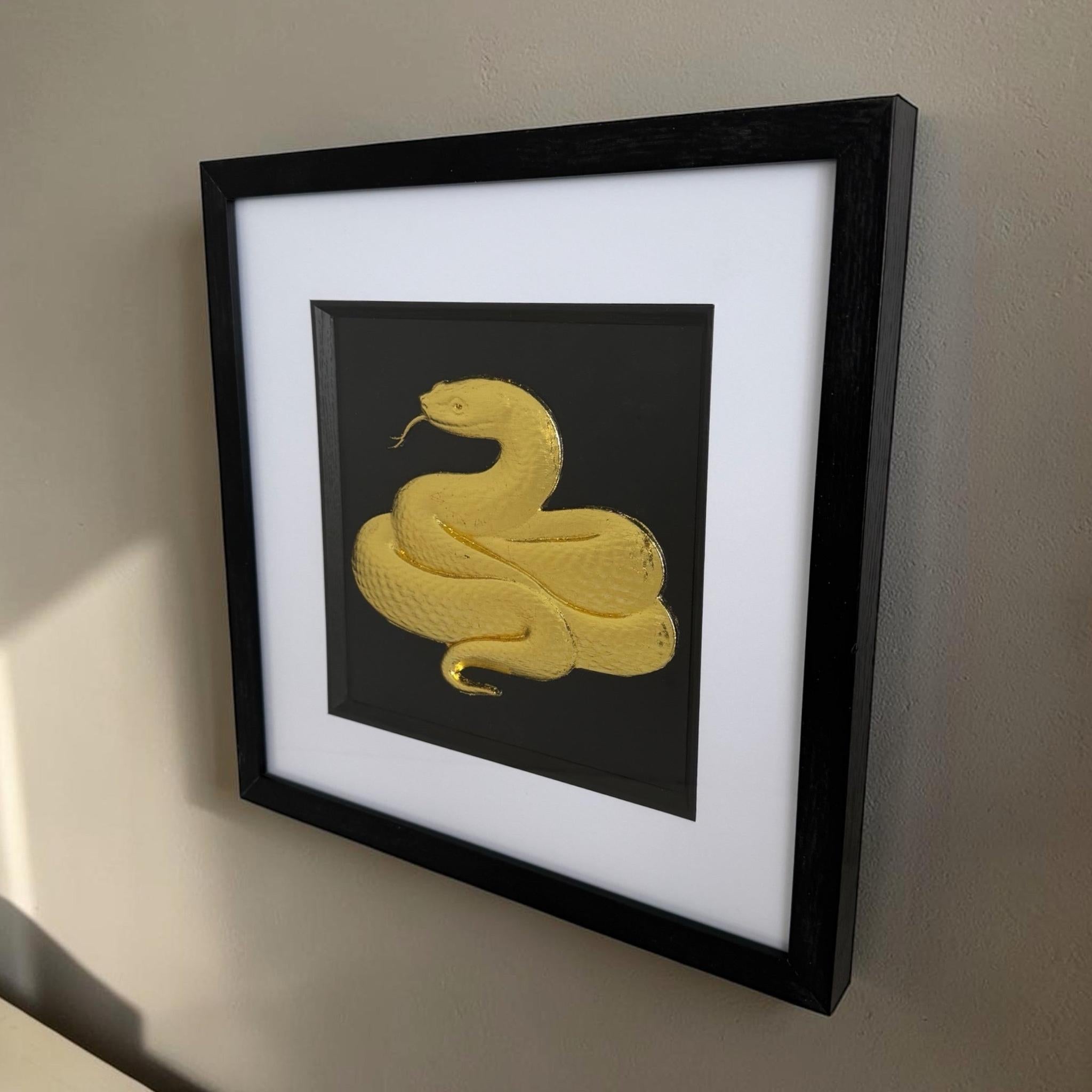 Angled gold framed snake artwork on a wall showing black box frame depth, white mount and raised relief.