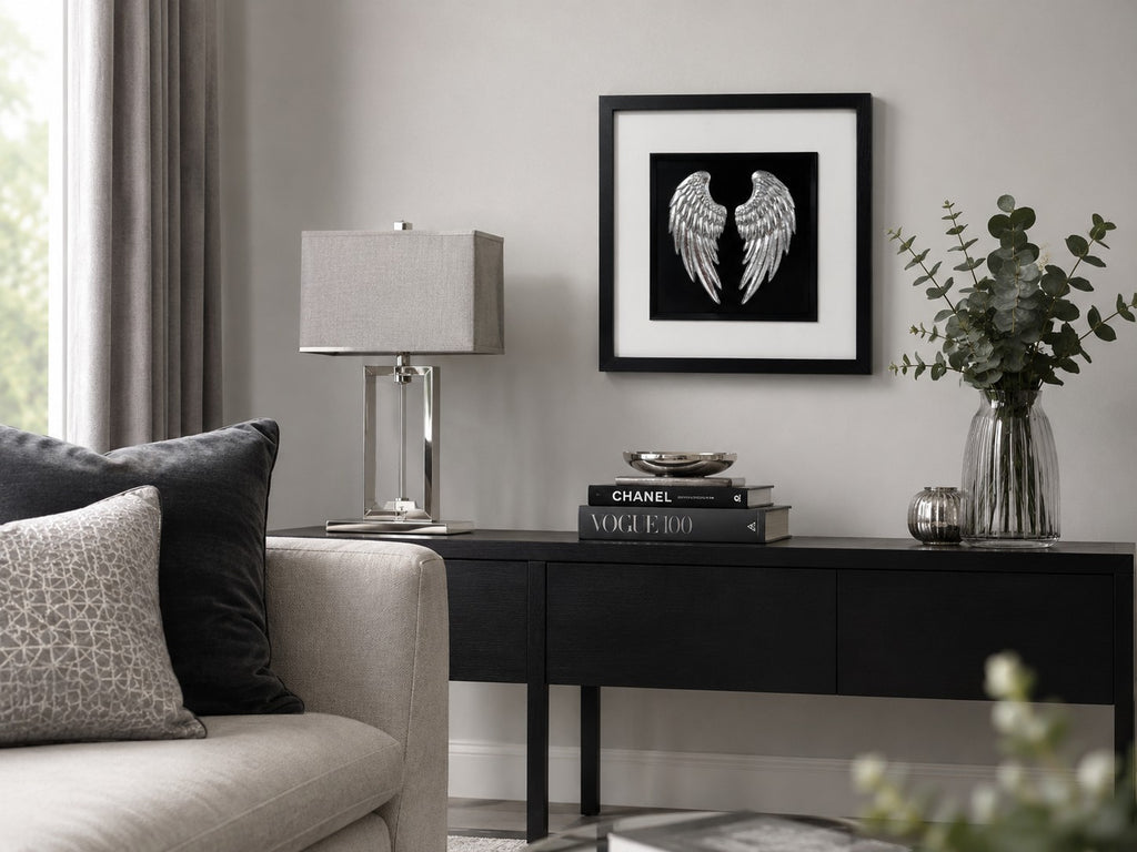 Framed angel wings wall art in gold leaf, styled on a neutral wall above a wooden sideboard with a vase of dried pampas and eucalyptus.