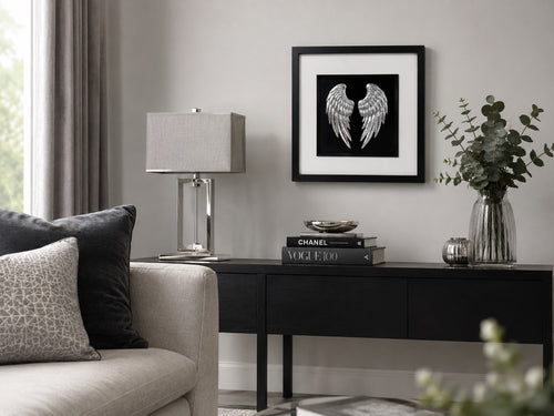 Framed angel wings wall art in gold leaf, styled on a neutral wall above a wooden sideboard with a vase of dried pampas and eucalyptus.