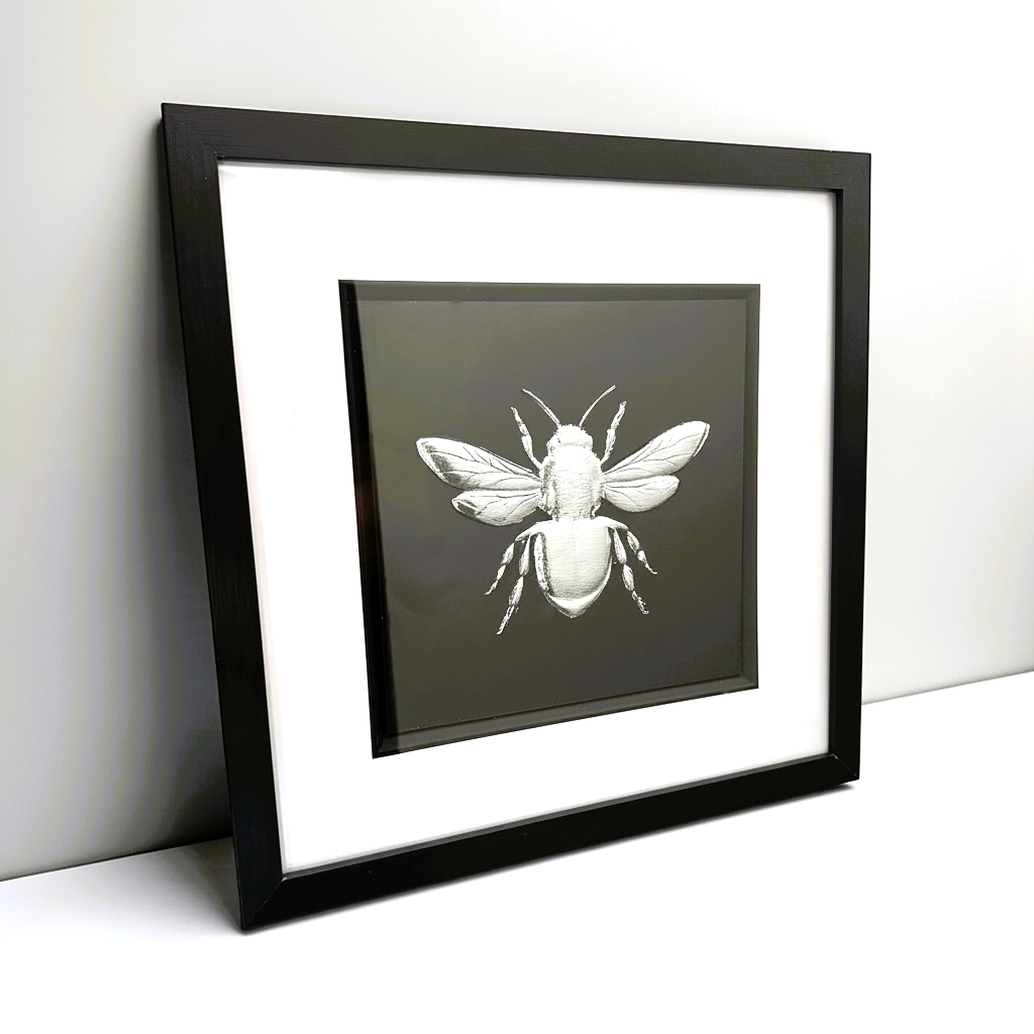 Front-facing silver leaf bumble bee wall art with black background and white mount