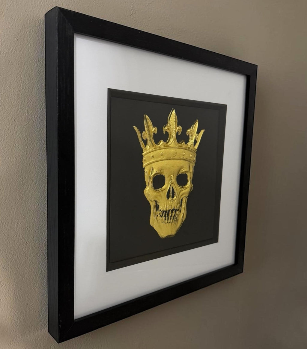 Angled gold crowned skull artwork on a wall showing black box frame depth and glass front.