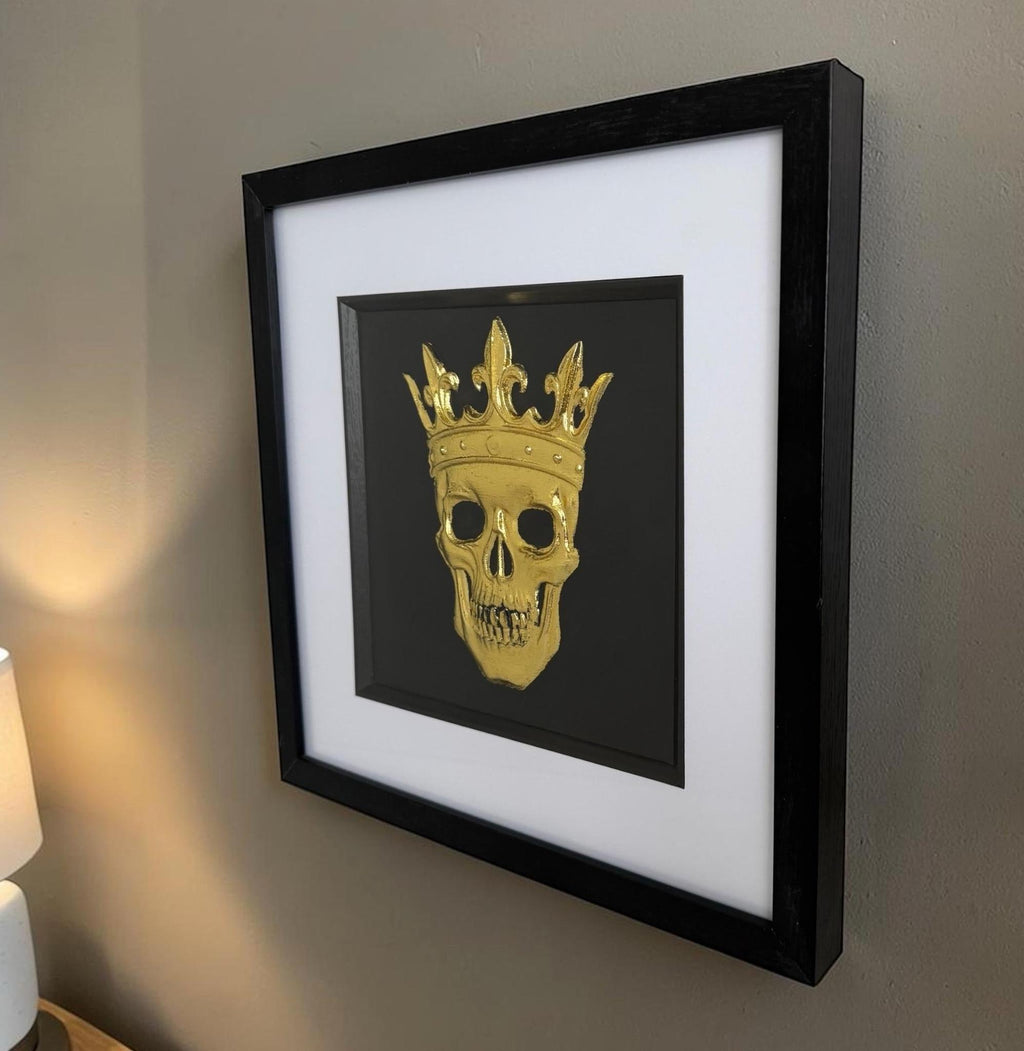 Gold framed crowned skull wall art on a neutral wall with black frame, white mount and raised relief.