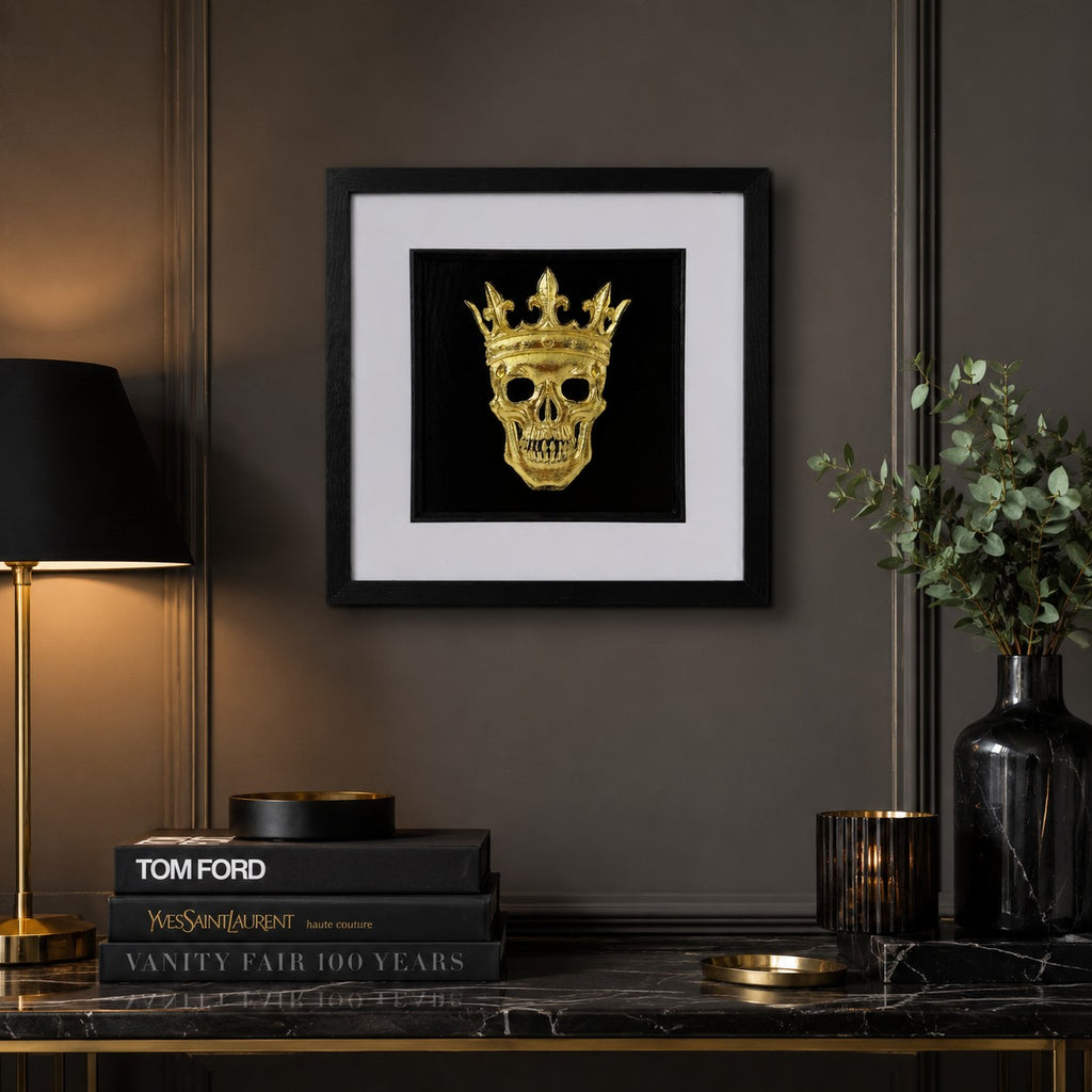 Gold crowned skull wall art styled in a dark gothic room with books, lamp, candle and black marble console.